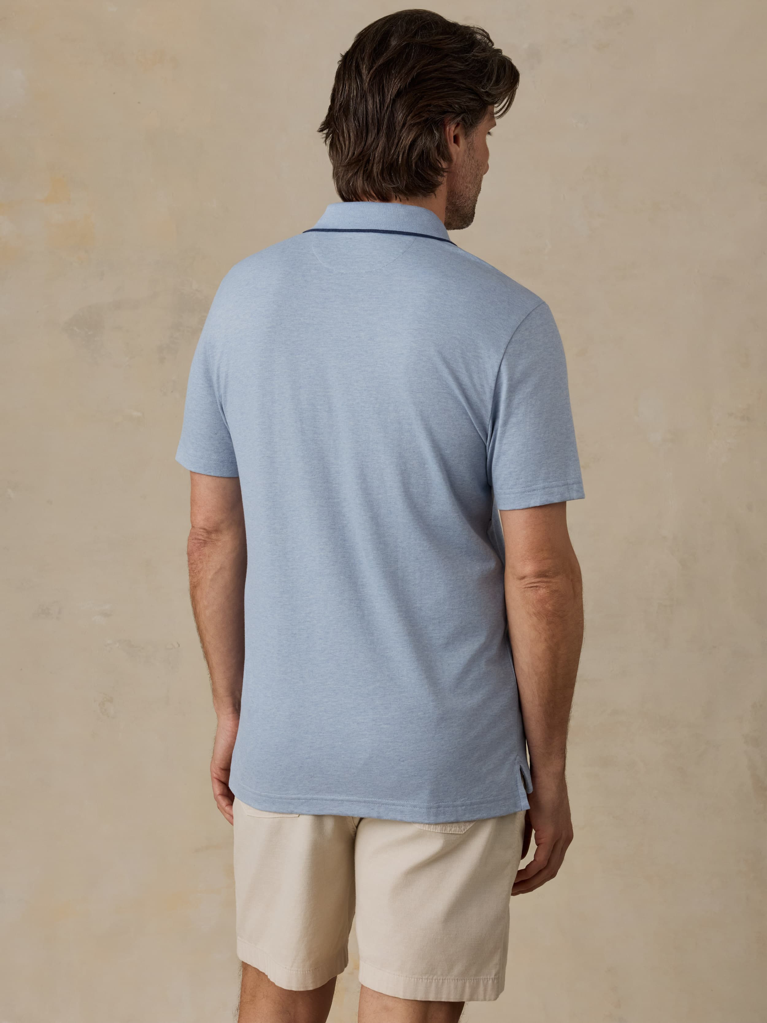 Man wearing a light blue polo shirt and beige shorts against a beige background