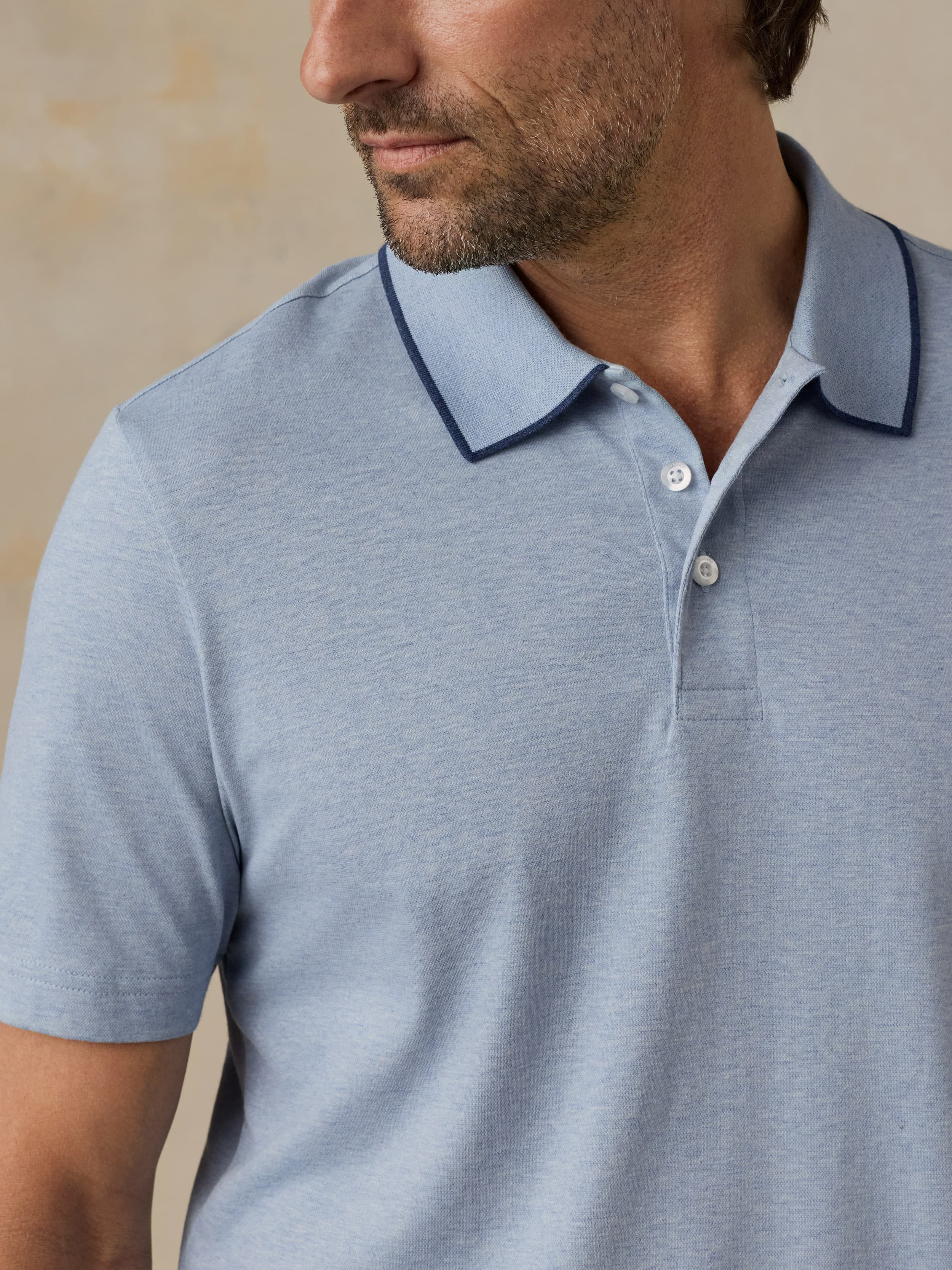 Man wearing a light blue polo shirt against a beige background