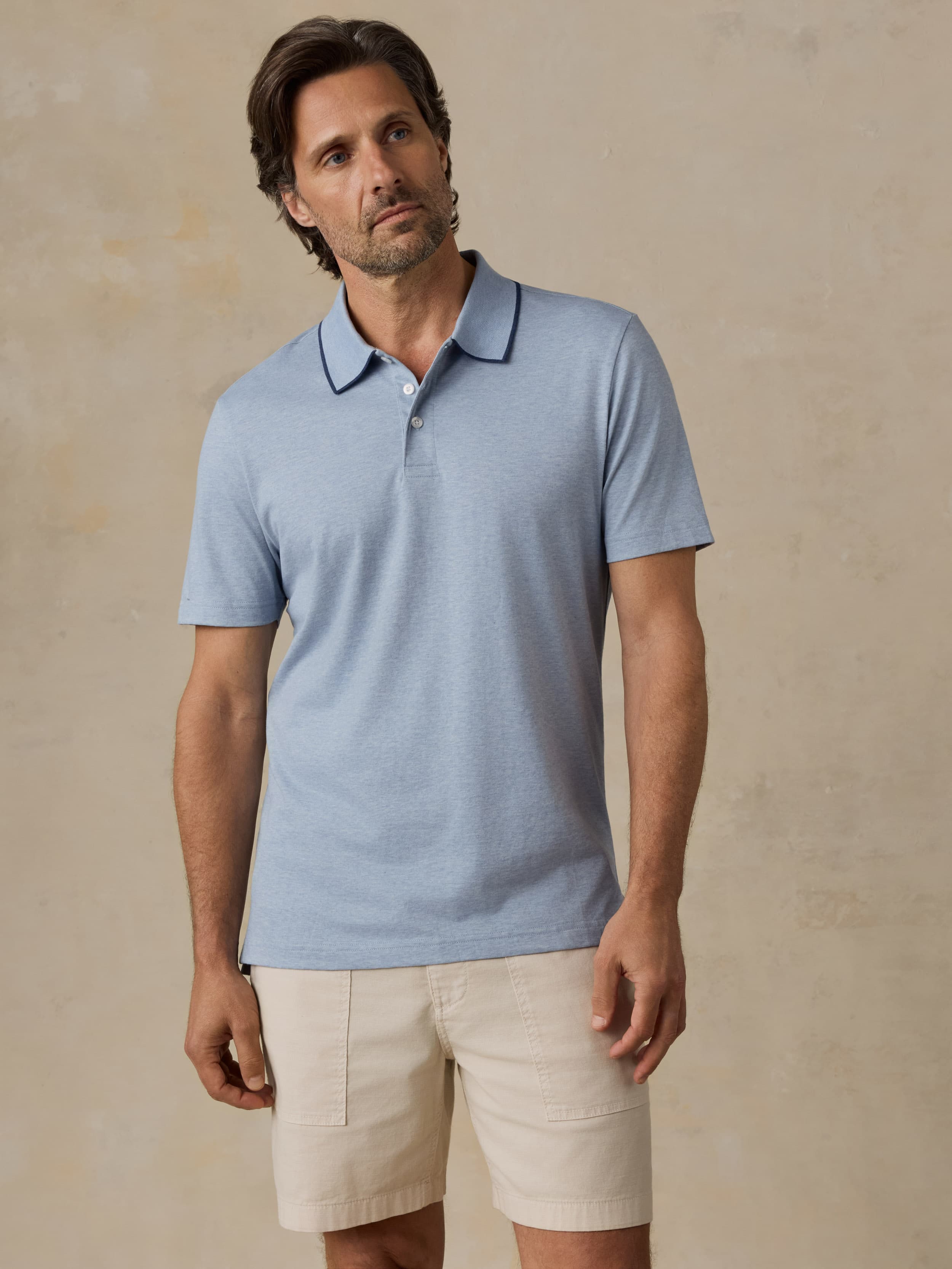 Man wearing a light blue polo shirt and beige shorts against a beige background
