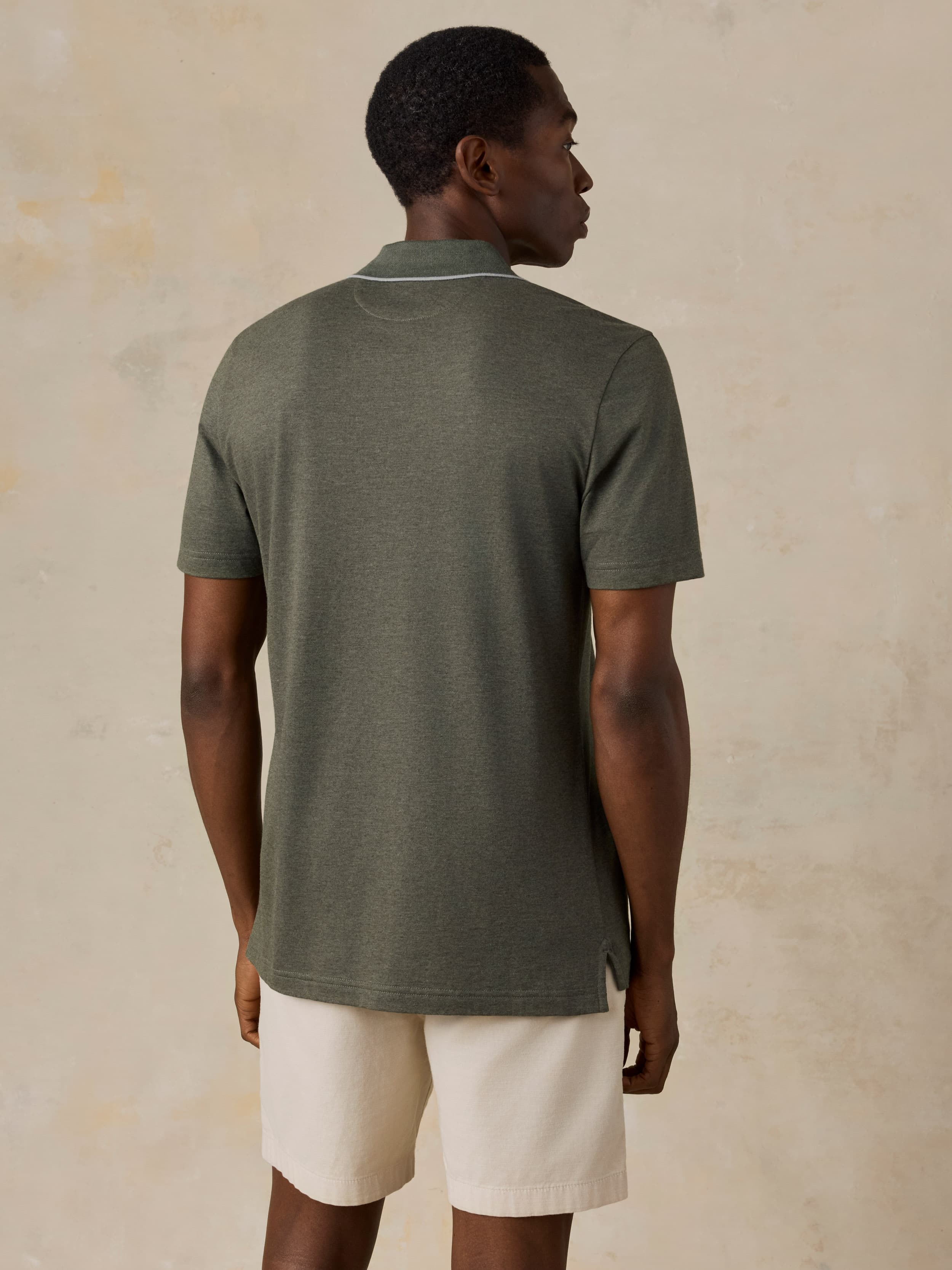 Man wearing a green polo and beige shorts against a beige background