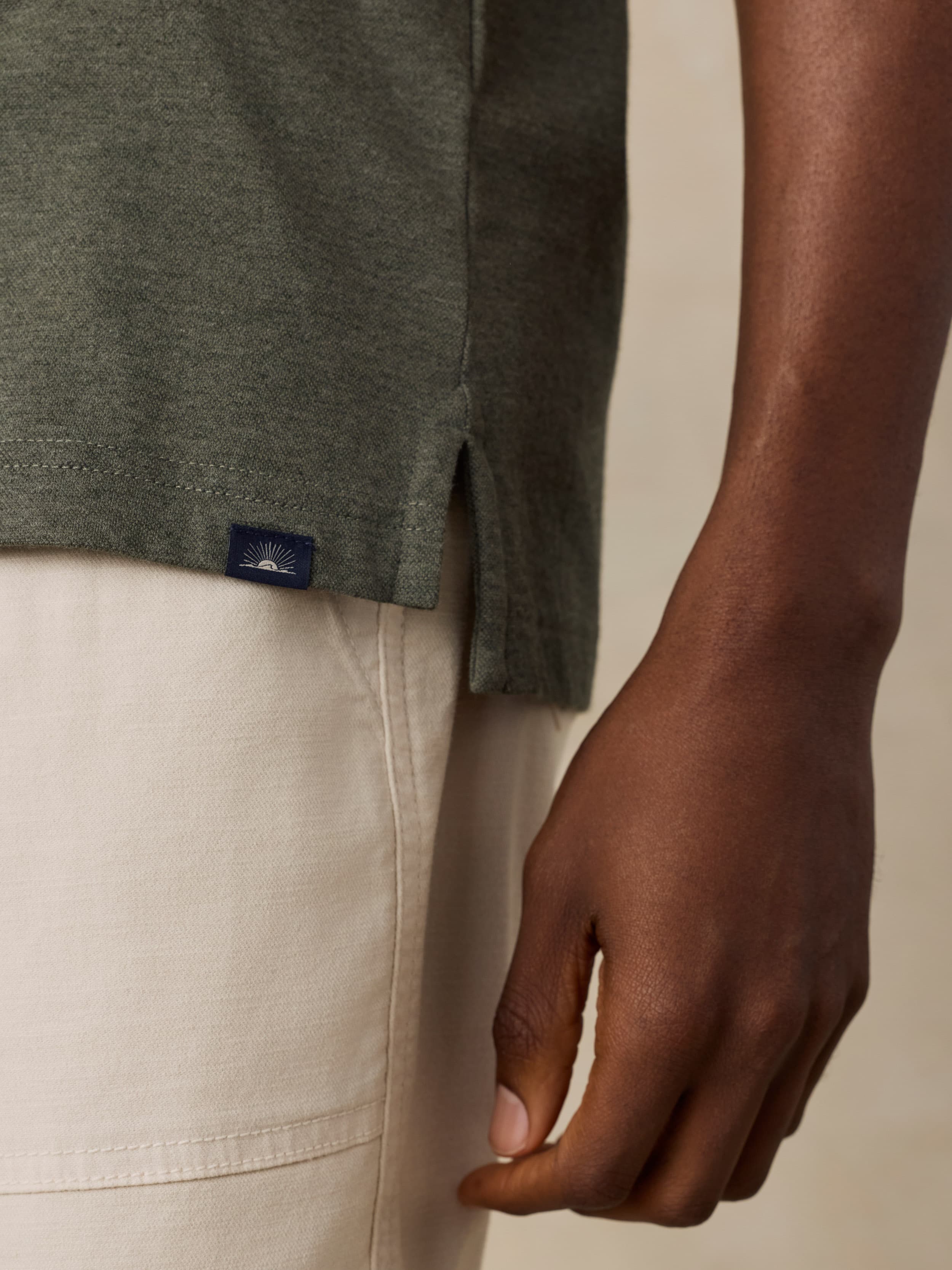 Close-up of a man wearing a green polo with a Faherty brand label near the hem against a beige background