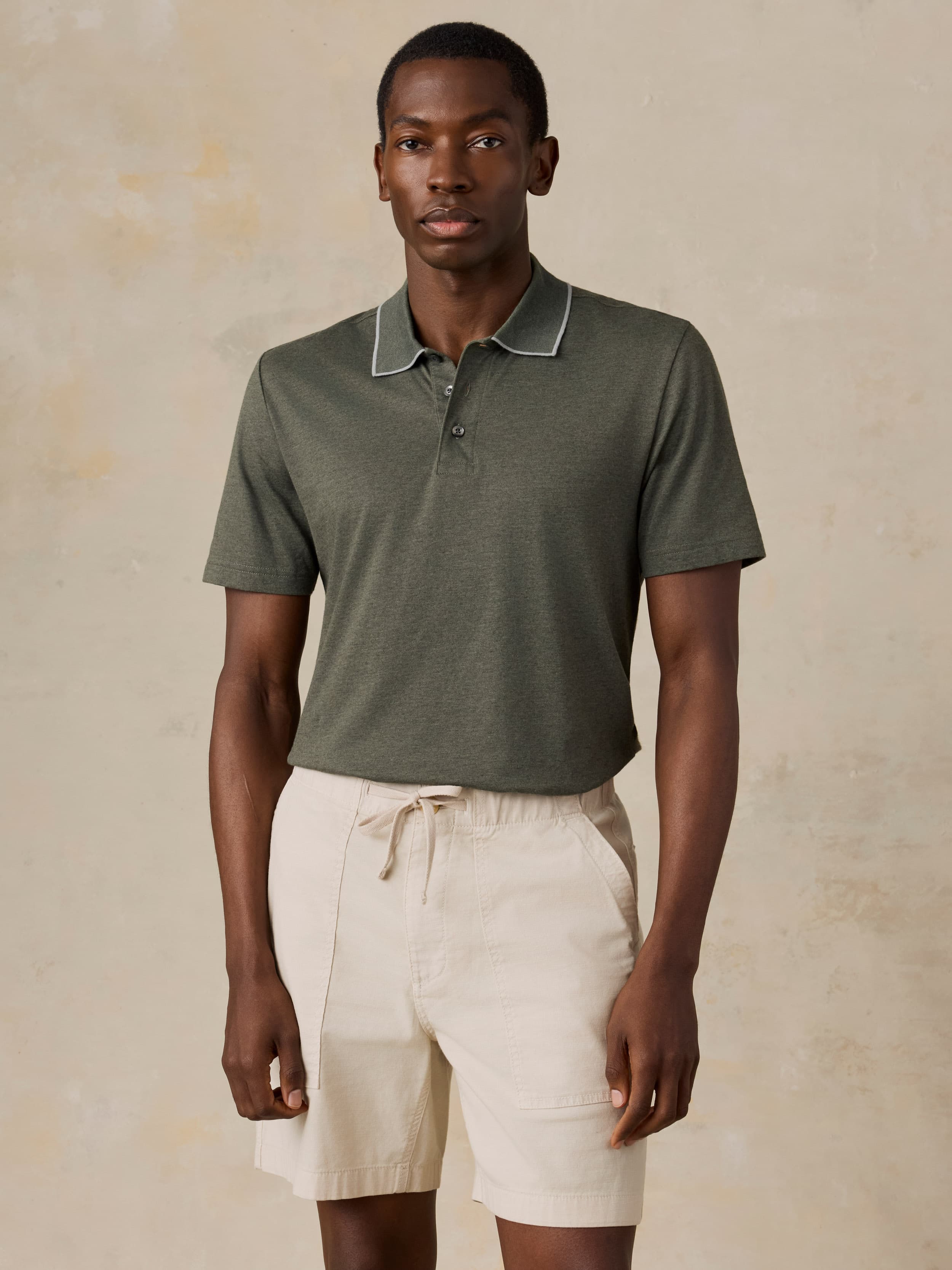 Man wearing a green polo and beige shorts against a beige background