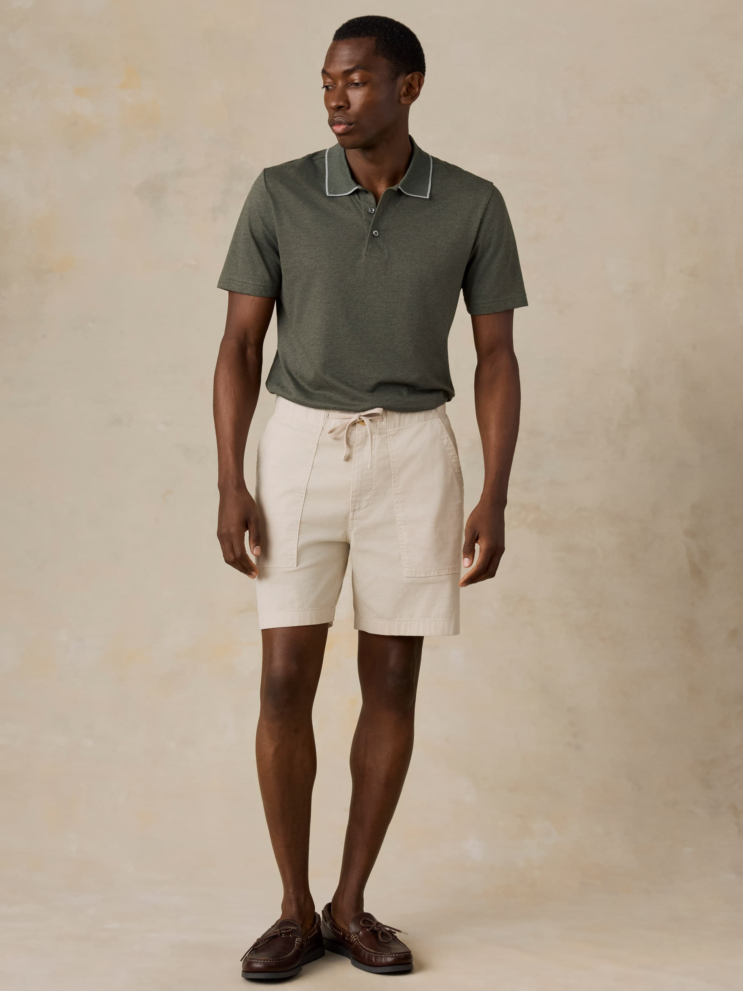 Man wearing a green polo and beige shorts against a beige background