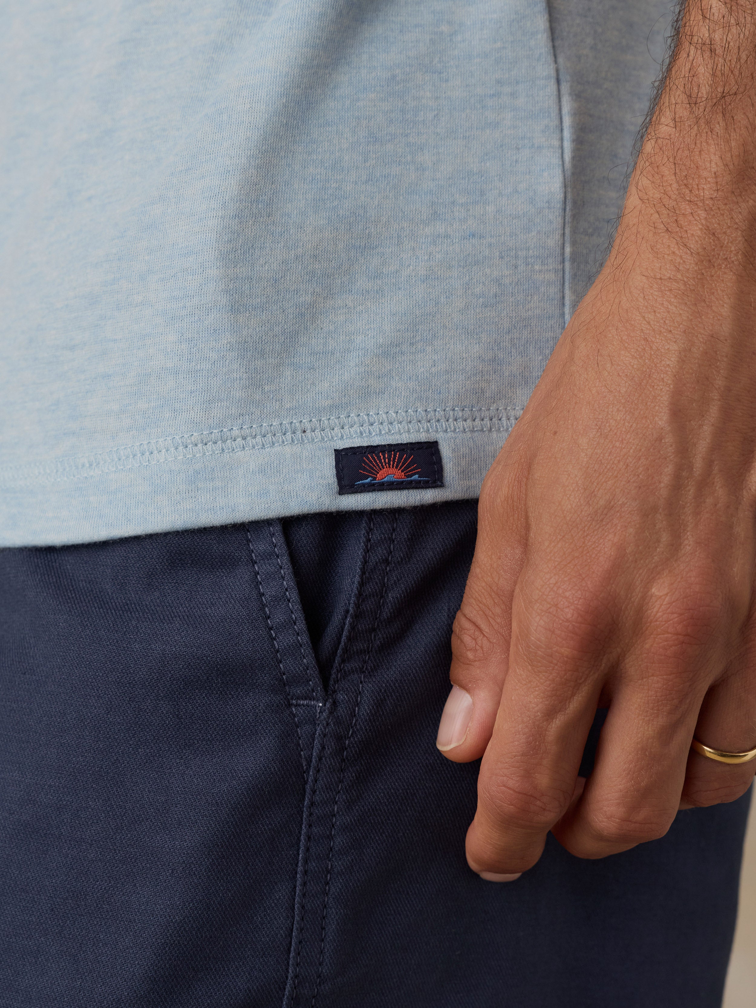 Close-up of a man wearing a light blue heather henley and navy blue shorts, with a small Faherty brand patch visible near the hem.