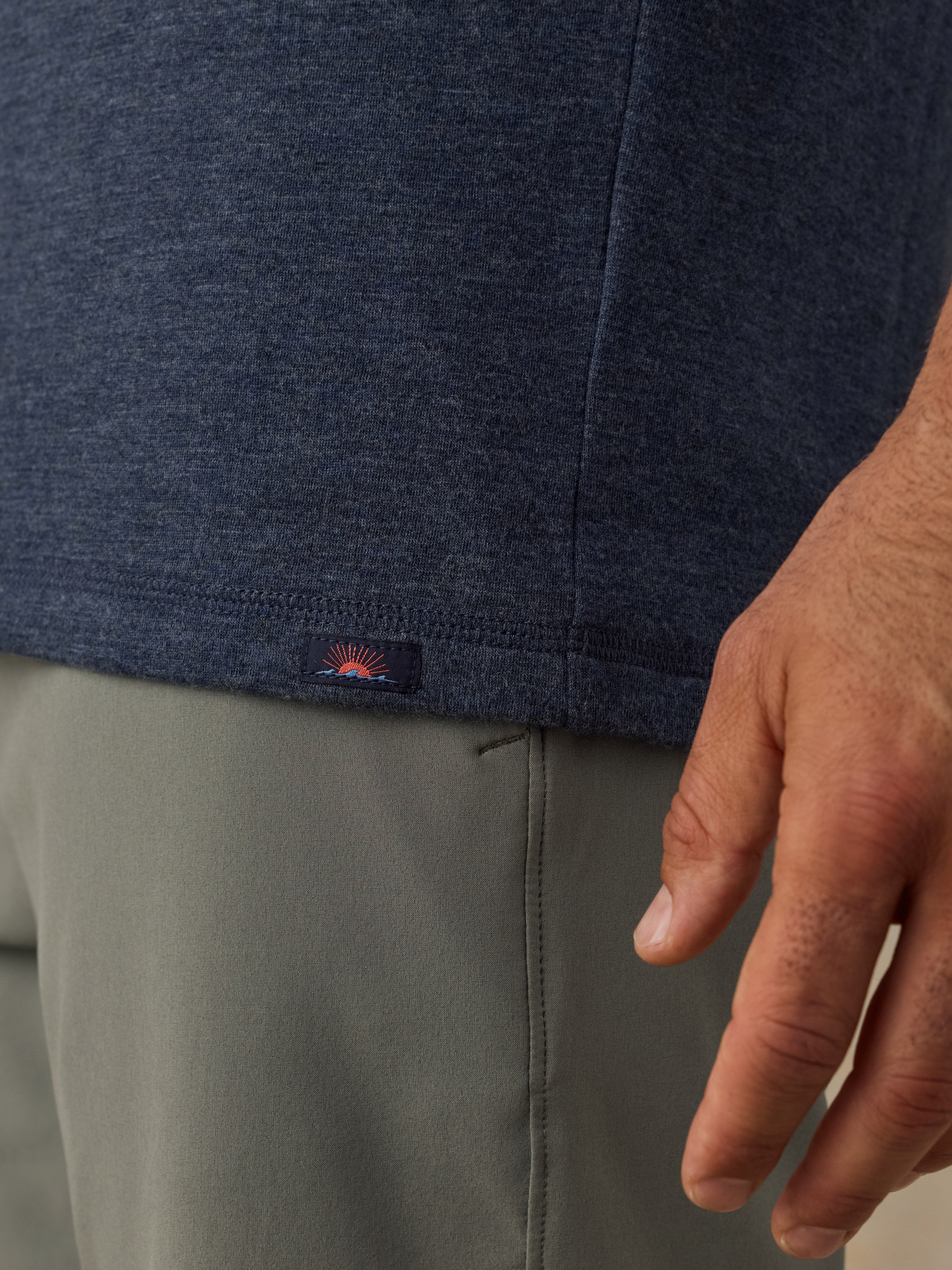 Close-up of a man wearing a heathered navy blue t-shirt and olive green shorts, with a small Faherty brand logo visible on the hem of the shirt.