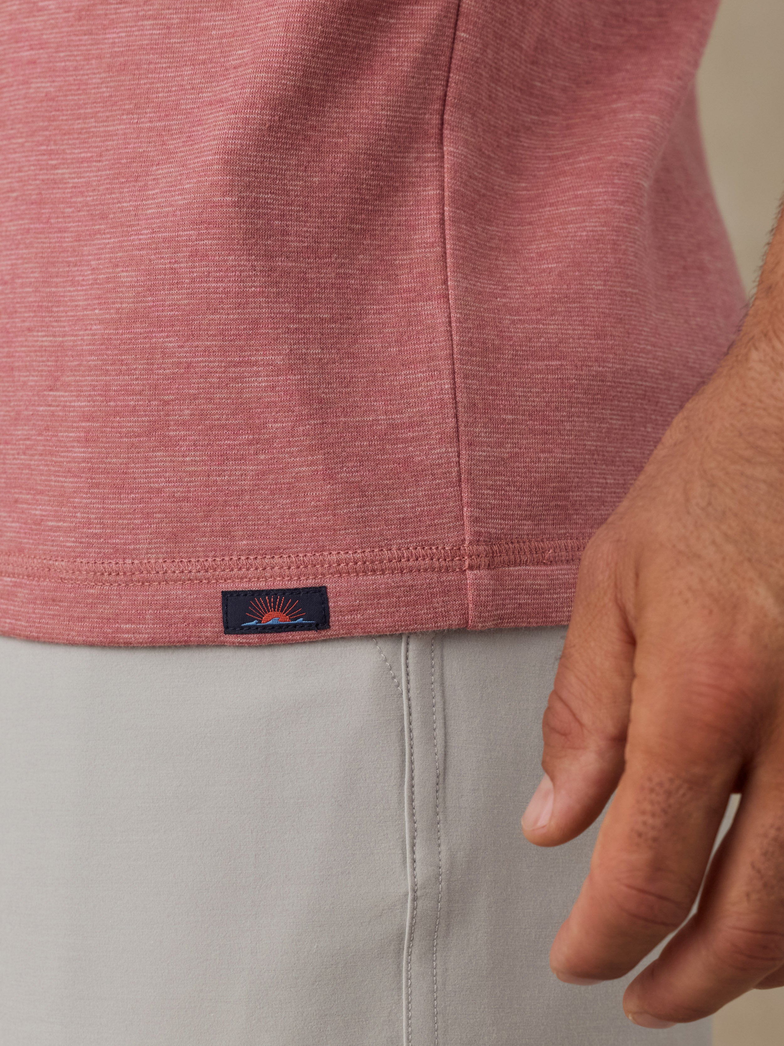 Close-up of a man wearing a heathered dusty pink short-sleeve top and light gray shorts, with a small Faherty brand tag near the hem.