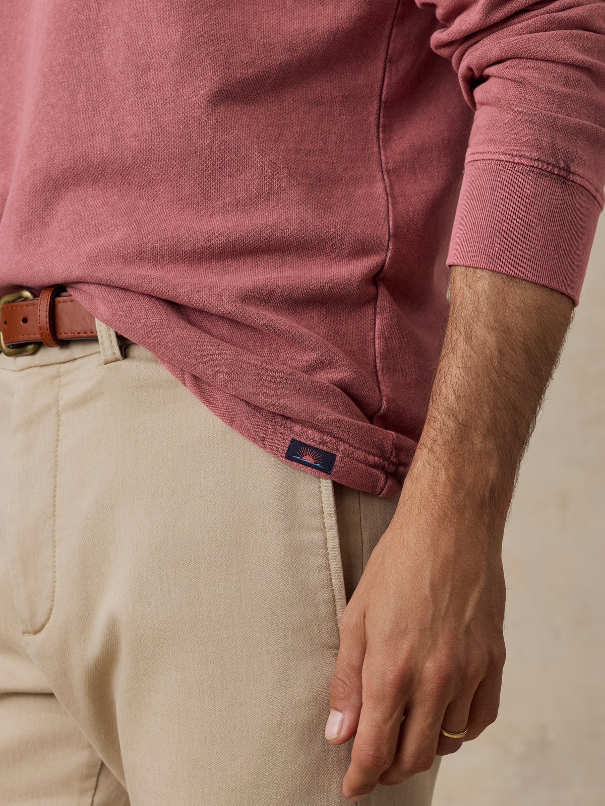A close-up of a person wearing a dusty rose long-sleeve shirt tucked into beige pants with a brown leather belt, showing the side hem and a small navy brand tab., image 5 of 7