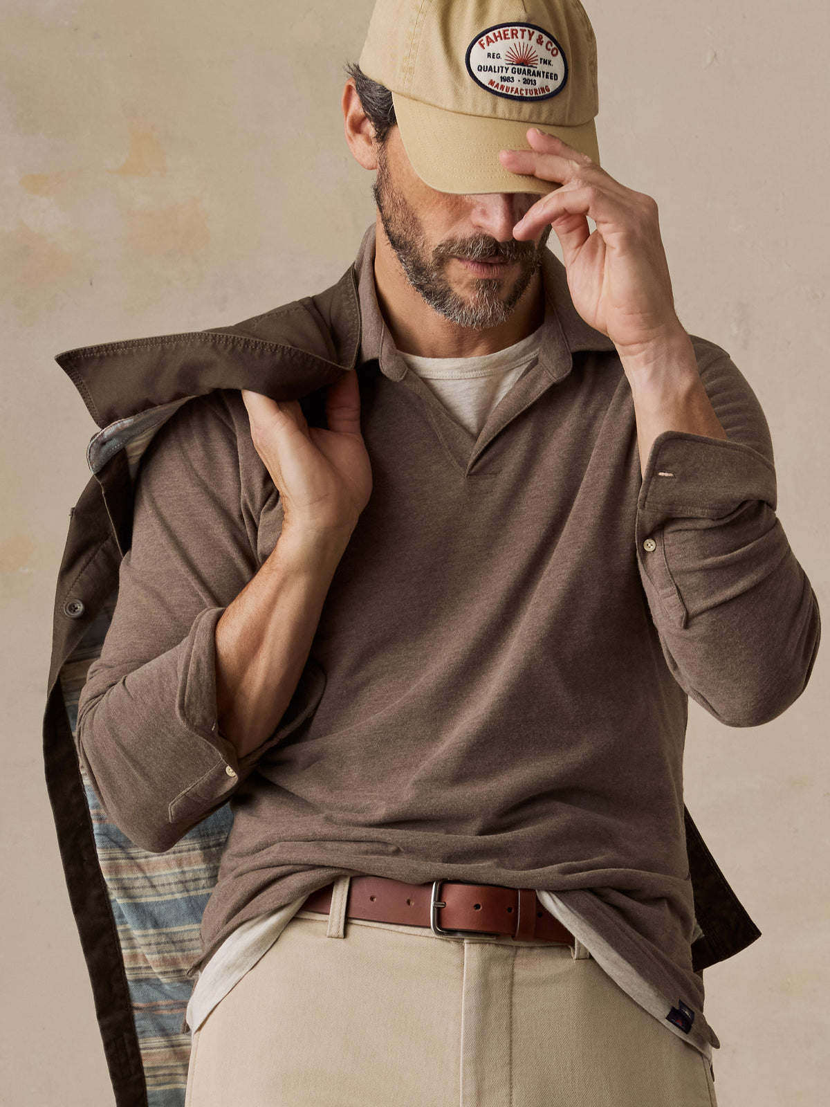 Close up of a man wearing a brown polo shirt, beige chino pants, beige hat, and a brown jacket, image 4 of 6