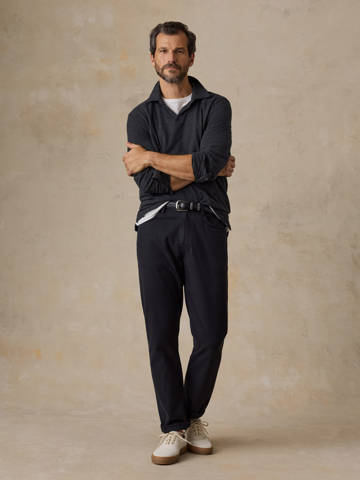 A man wearing a dark grey sweater polo, black chino pants, and white sneakers, image 6 of 6