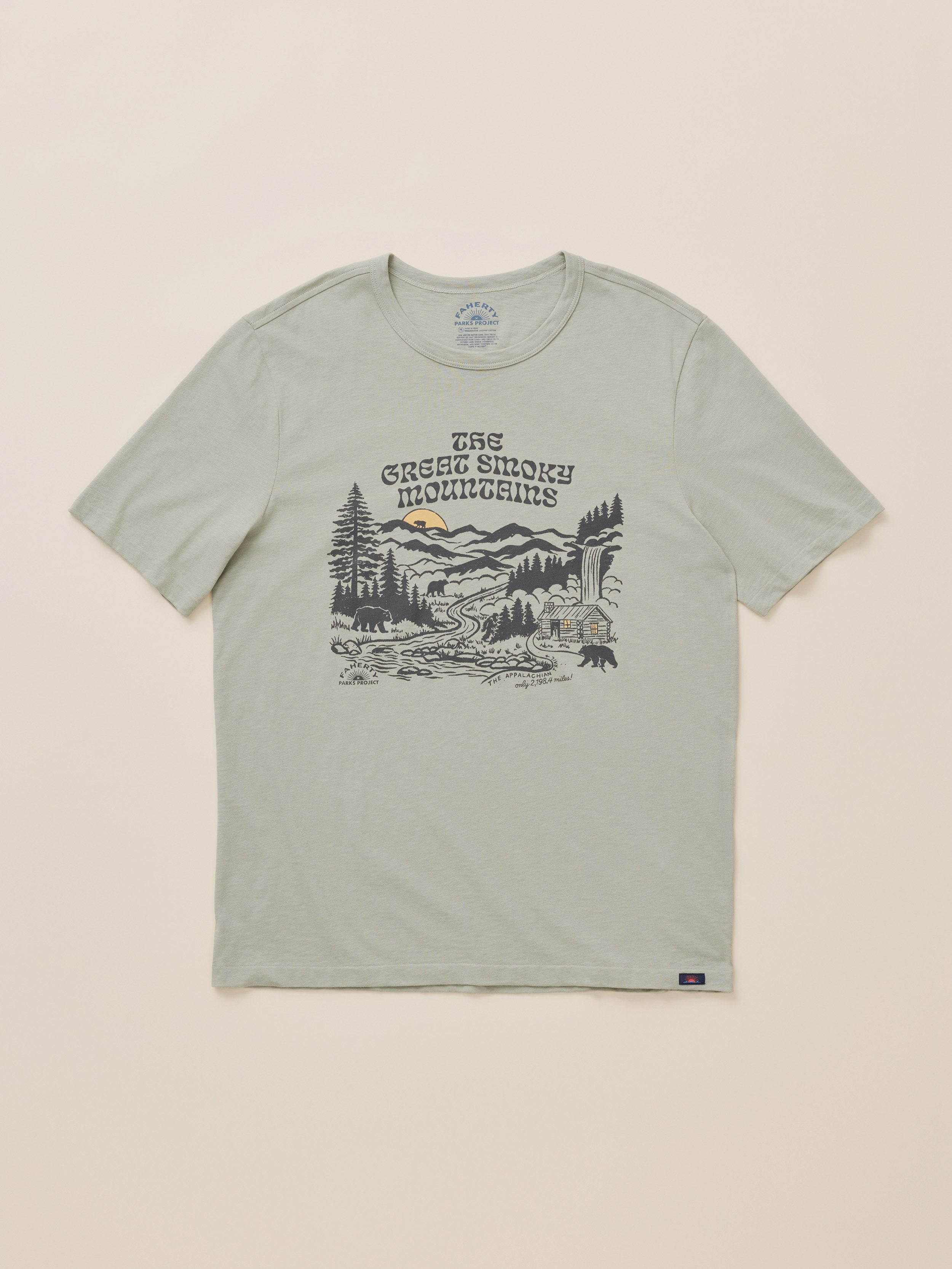 A light sage green crewneck t-shirt featuring a detailed black and gray graphic of a mountain landscape with the text 'The Great Smoky Mountains' printed on the chest, displayed flat against a light beige background.