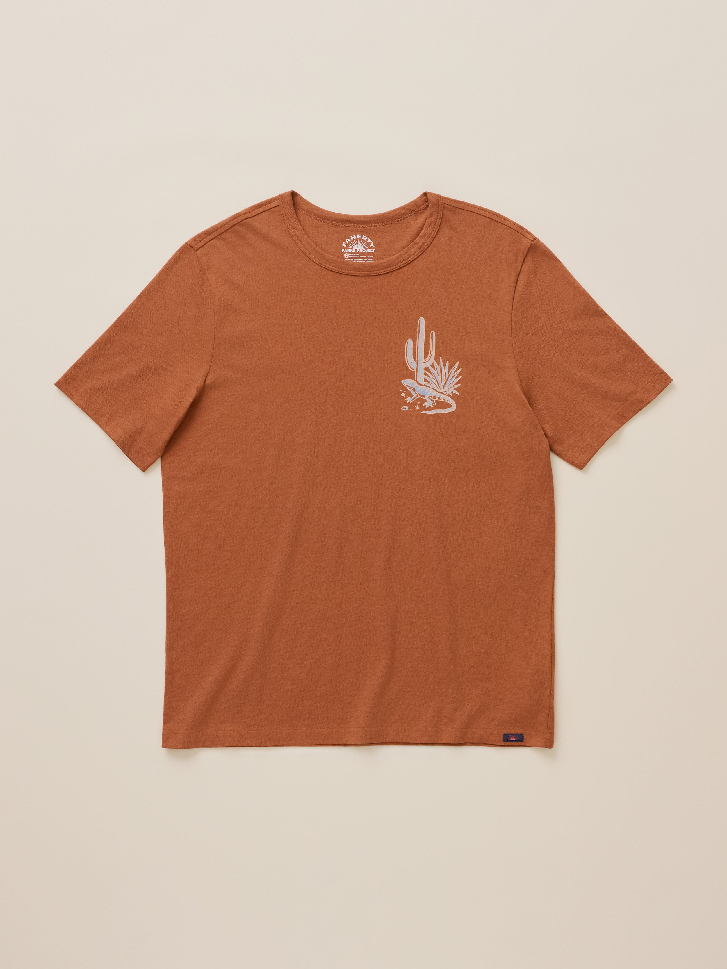 A rust-colored short-sleeve t-shirt with a small white desert cactus graphic on the left chest, displayed flat against a light beige background.
