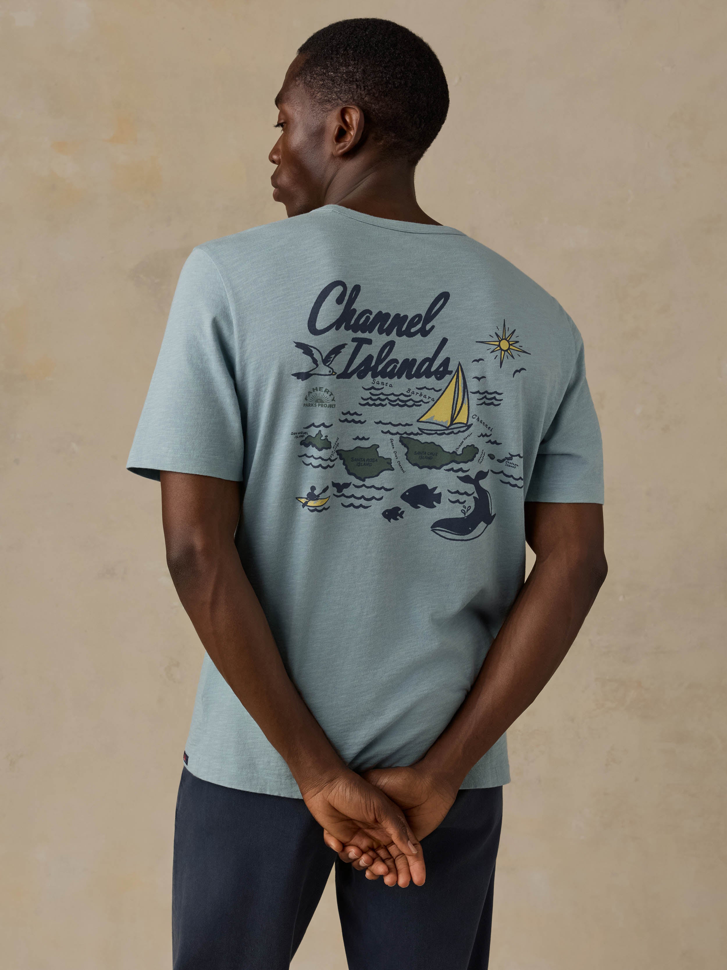 Man wearing a blue t-shirt with Channel Islands graphic on the back and blue pants against a beige background