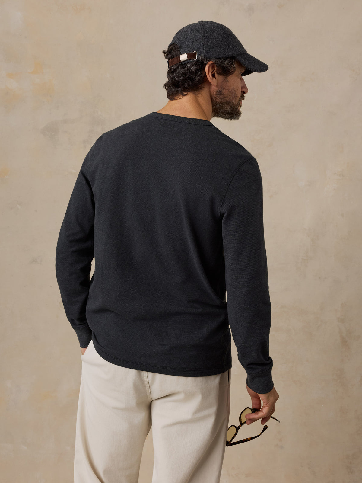 A man viewed from behind wearing a black henley and chino pants, image 6 of 6