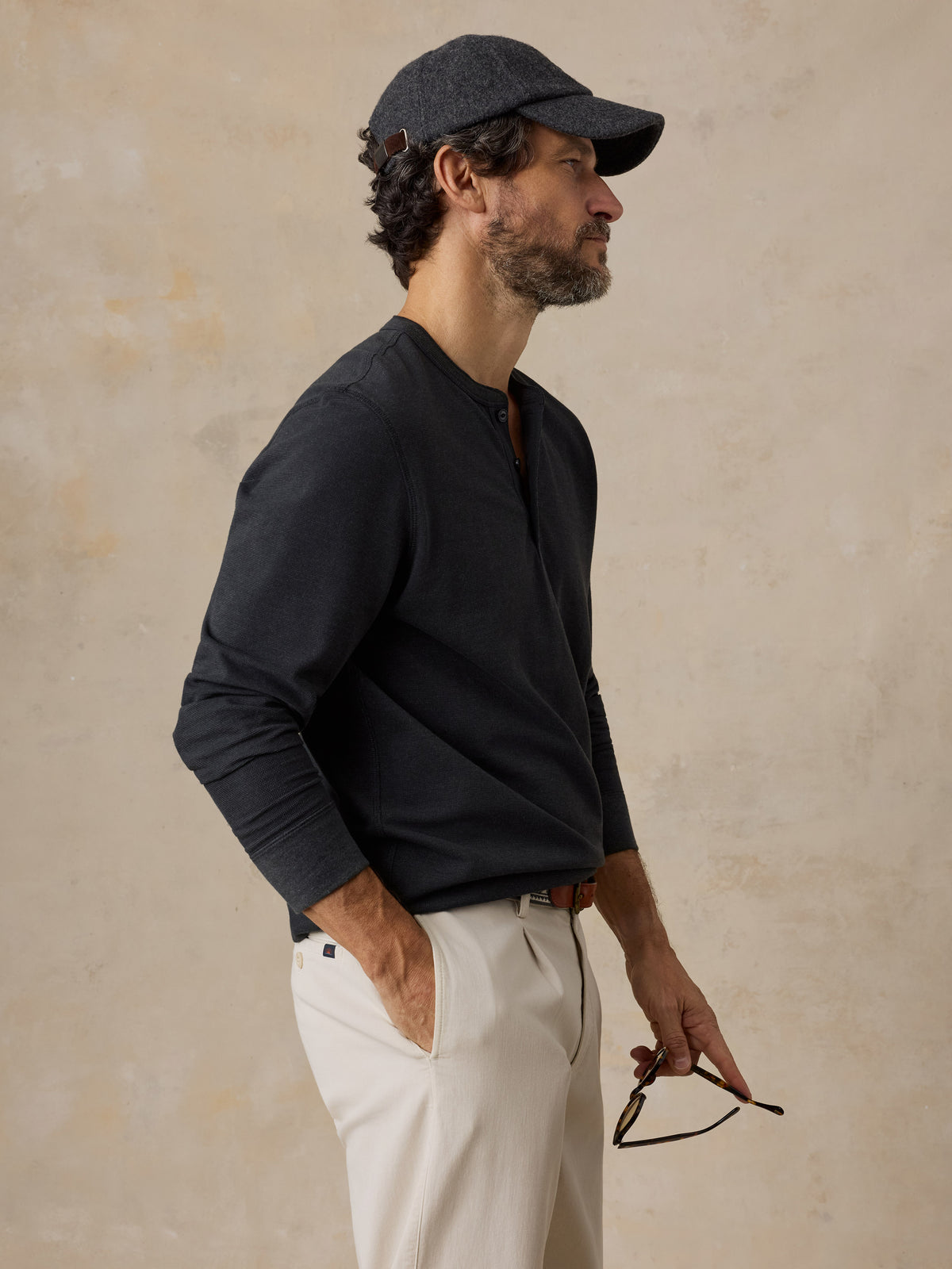 A man wearing a black henley and chino pants, image 3 of 6
