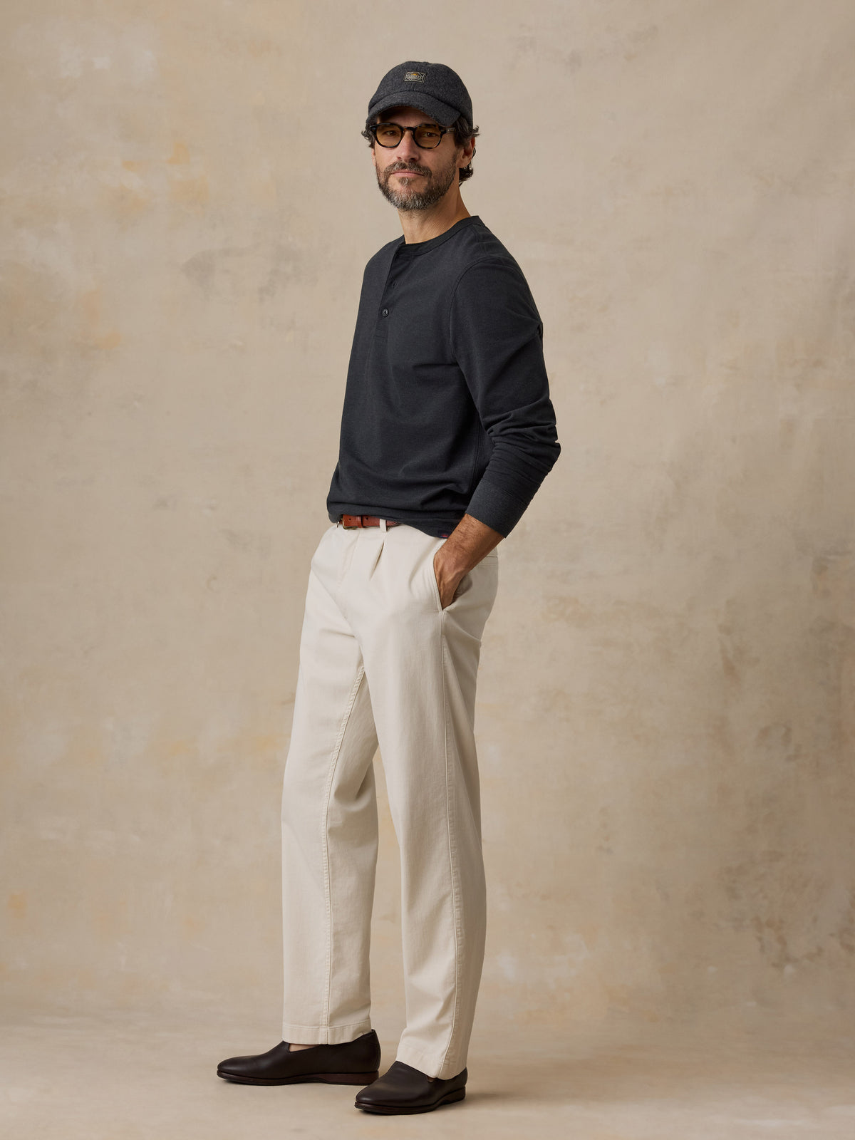 A man wearing a black henley and chino pants, image 2 of 6