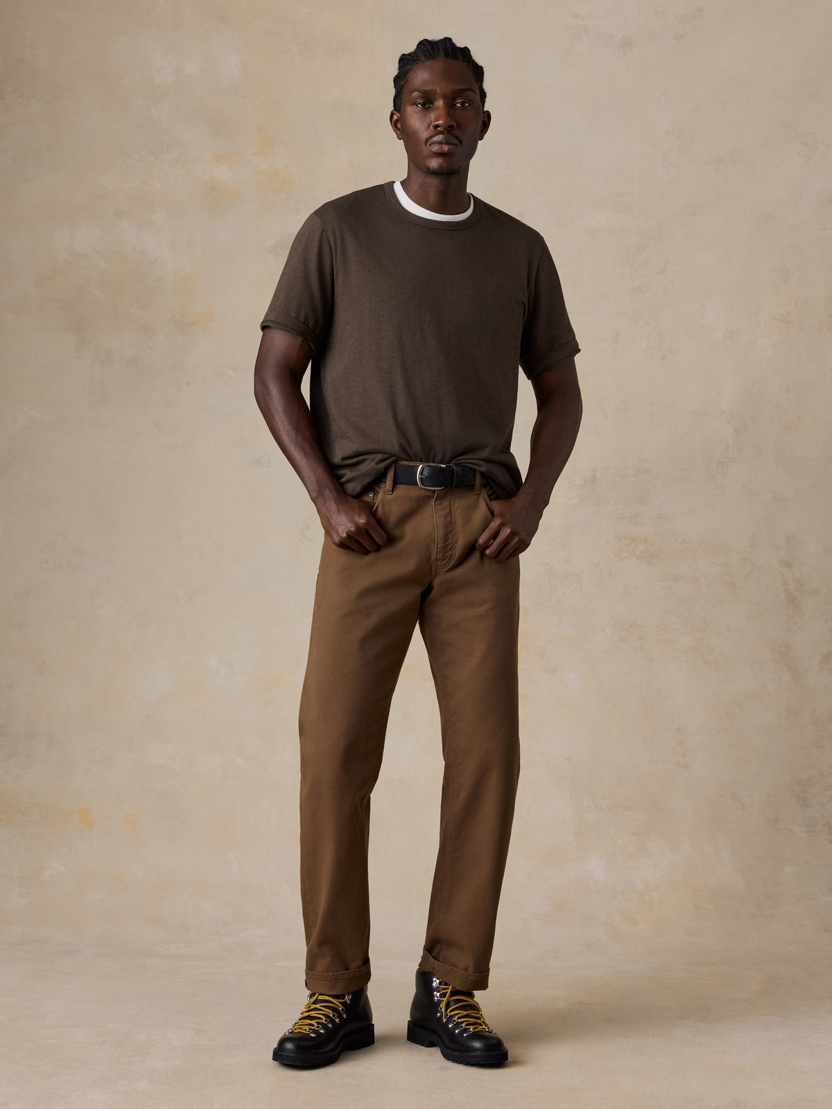 A man wearing a brown t-shirt, brown pants, and black boots, image 6 of 6
