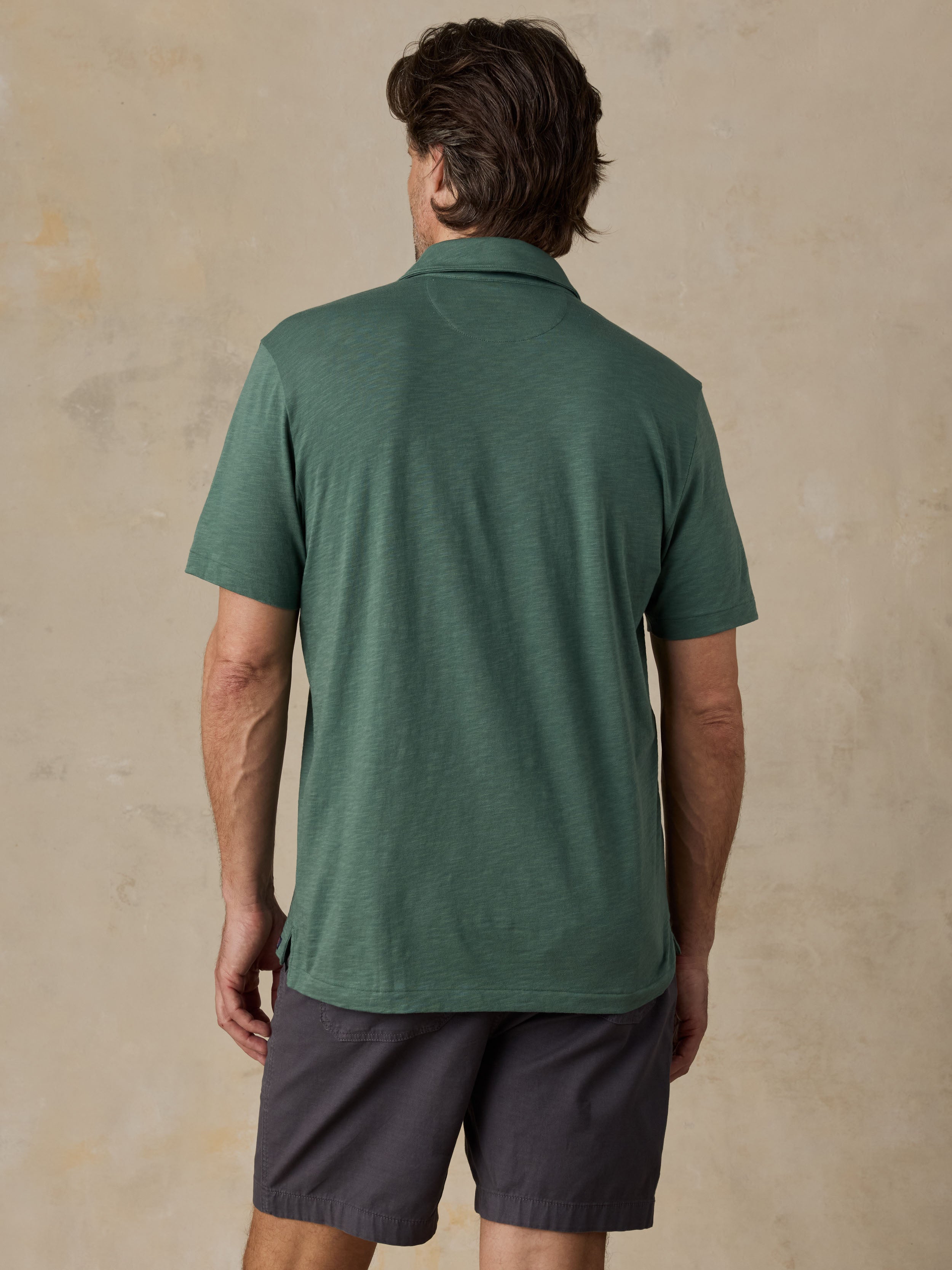Man wearing a green polo shirt and dark shorts against a beige background