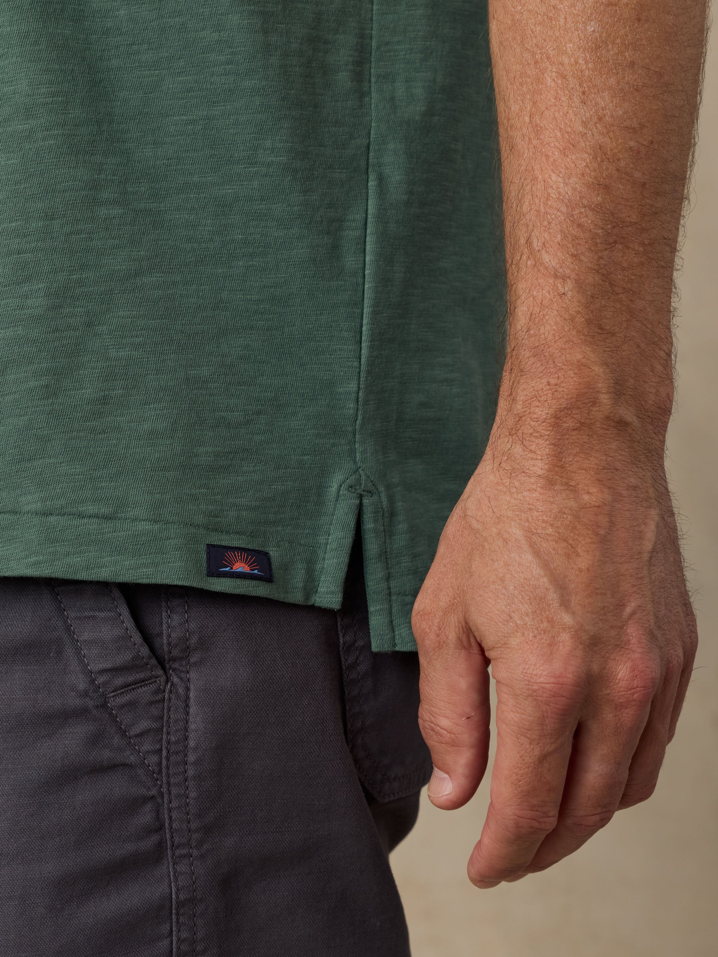 Close-up of a man wearing a green polo shirt with a visible Faherty brand logo and dark shorts