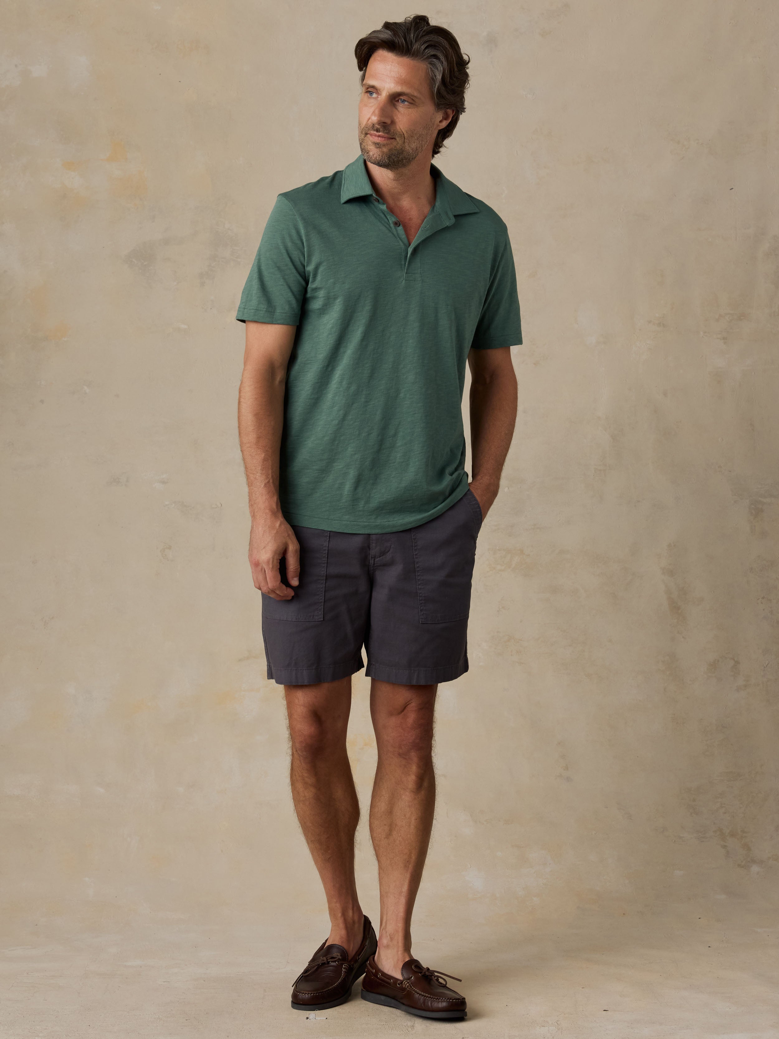 Man wearing a green polo shirt and dark shorts against a beige background