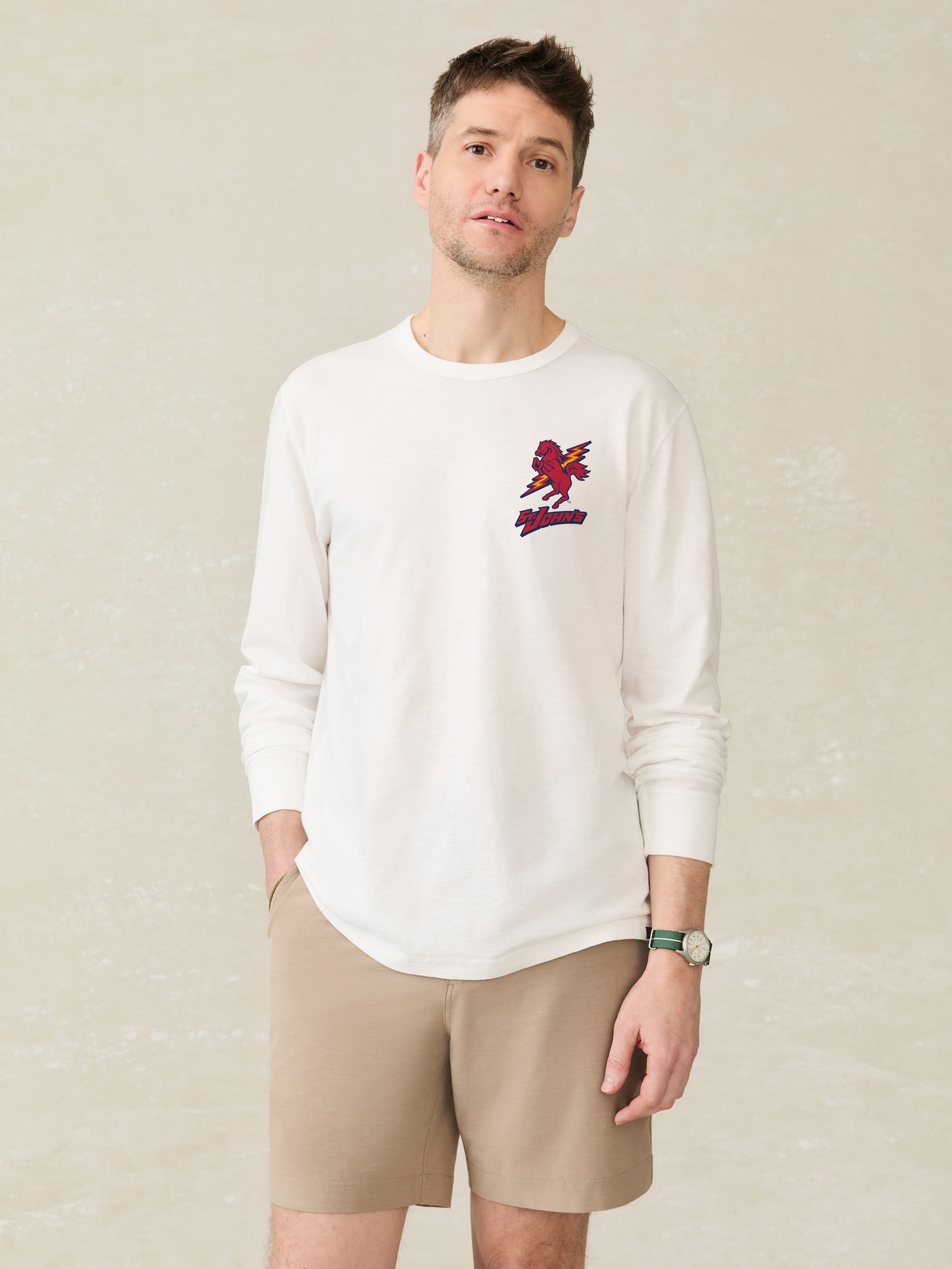 Man wearing a white long-sleeve crew neck t-shirt with St. John's embroidery on the chest, paired with beige shorts.