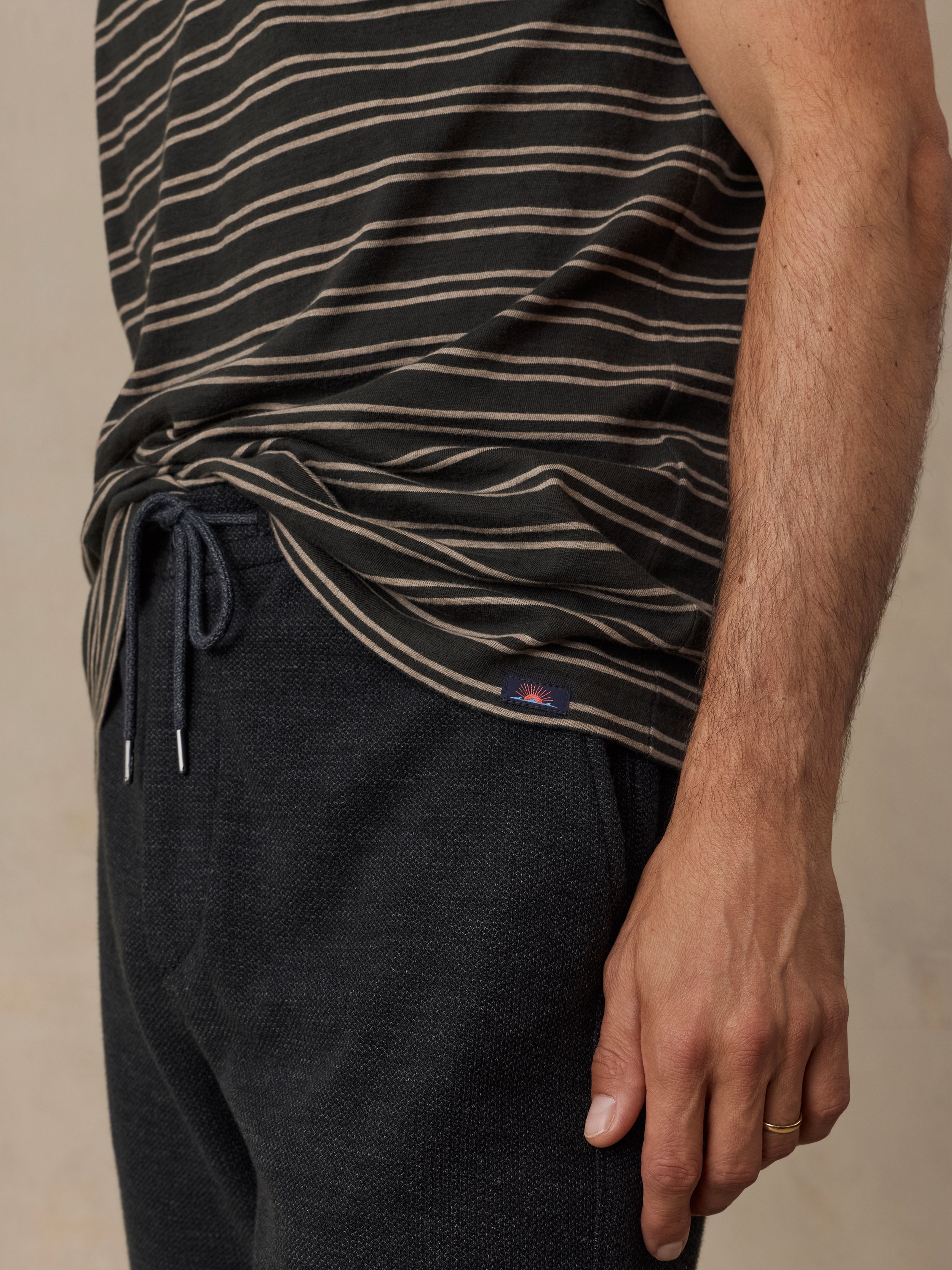 Close-up of a man wearing a black striped t-shirt and dark charcoal knit pants against a beige studio background