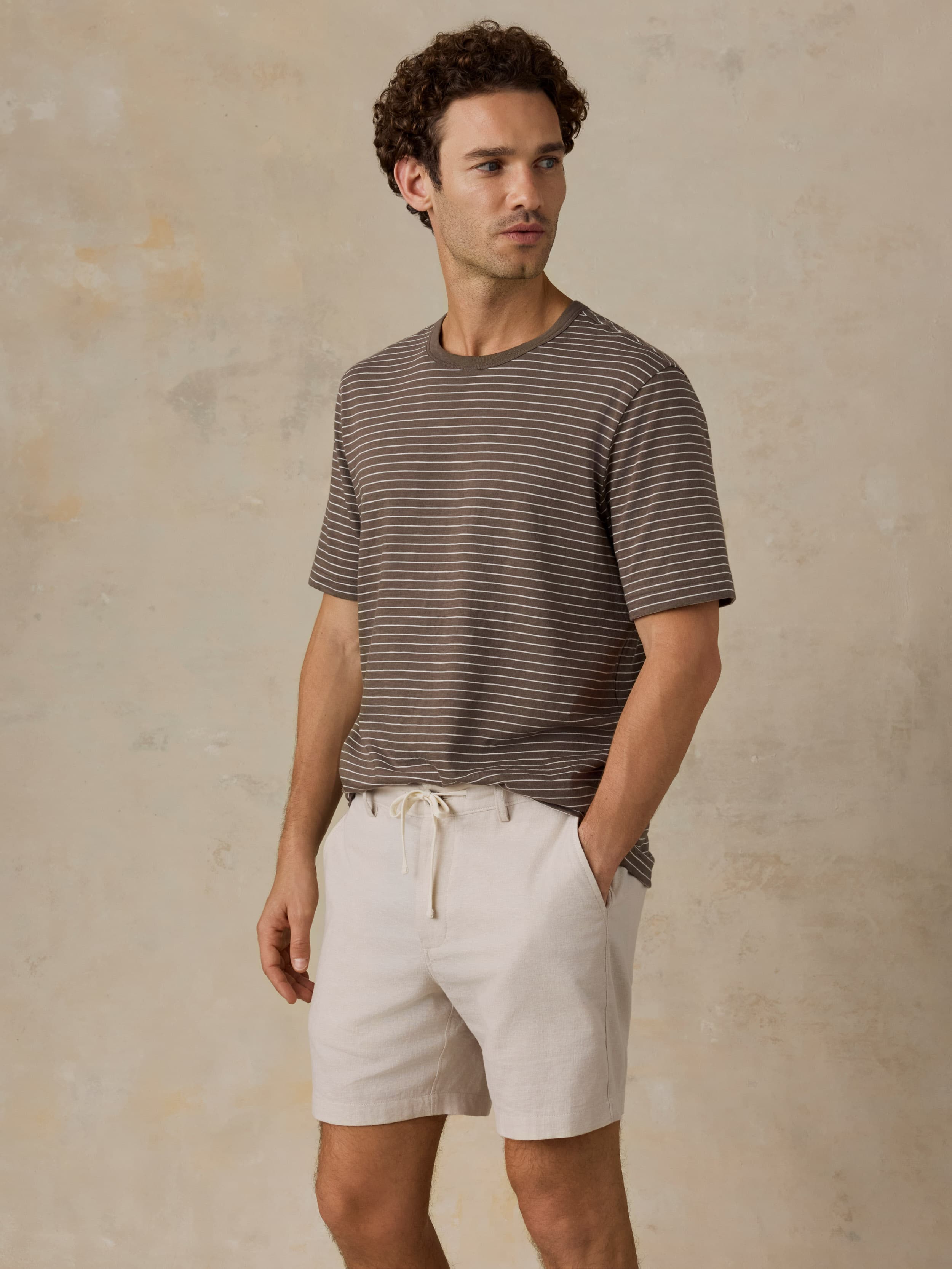 Man wearing a brown striped t-shirt and beige shorts against a beige background