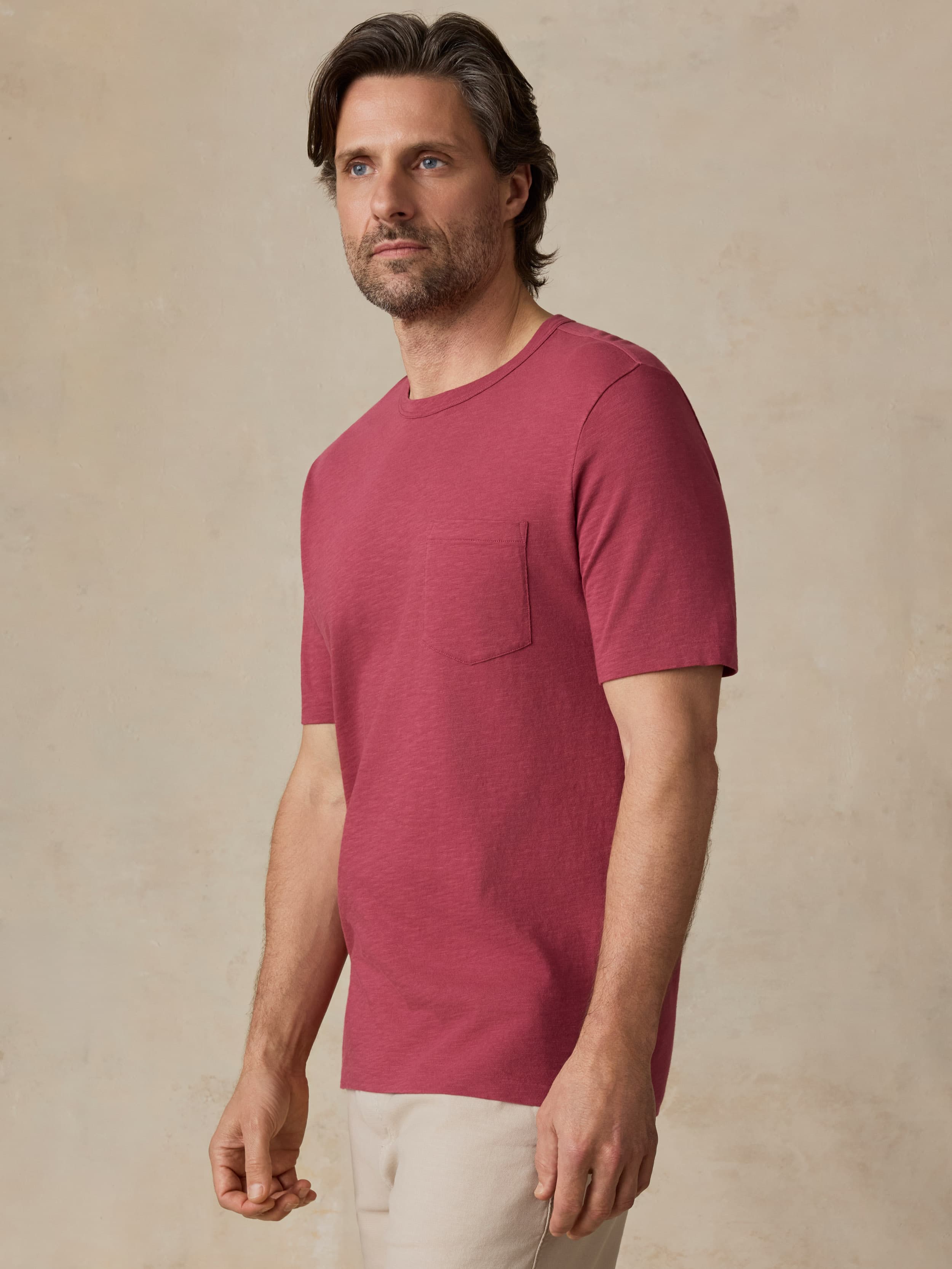 Man wearing a red t-shirt and beige shorts against a beige background