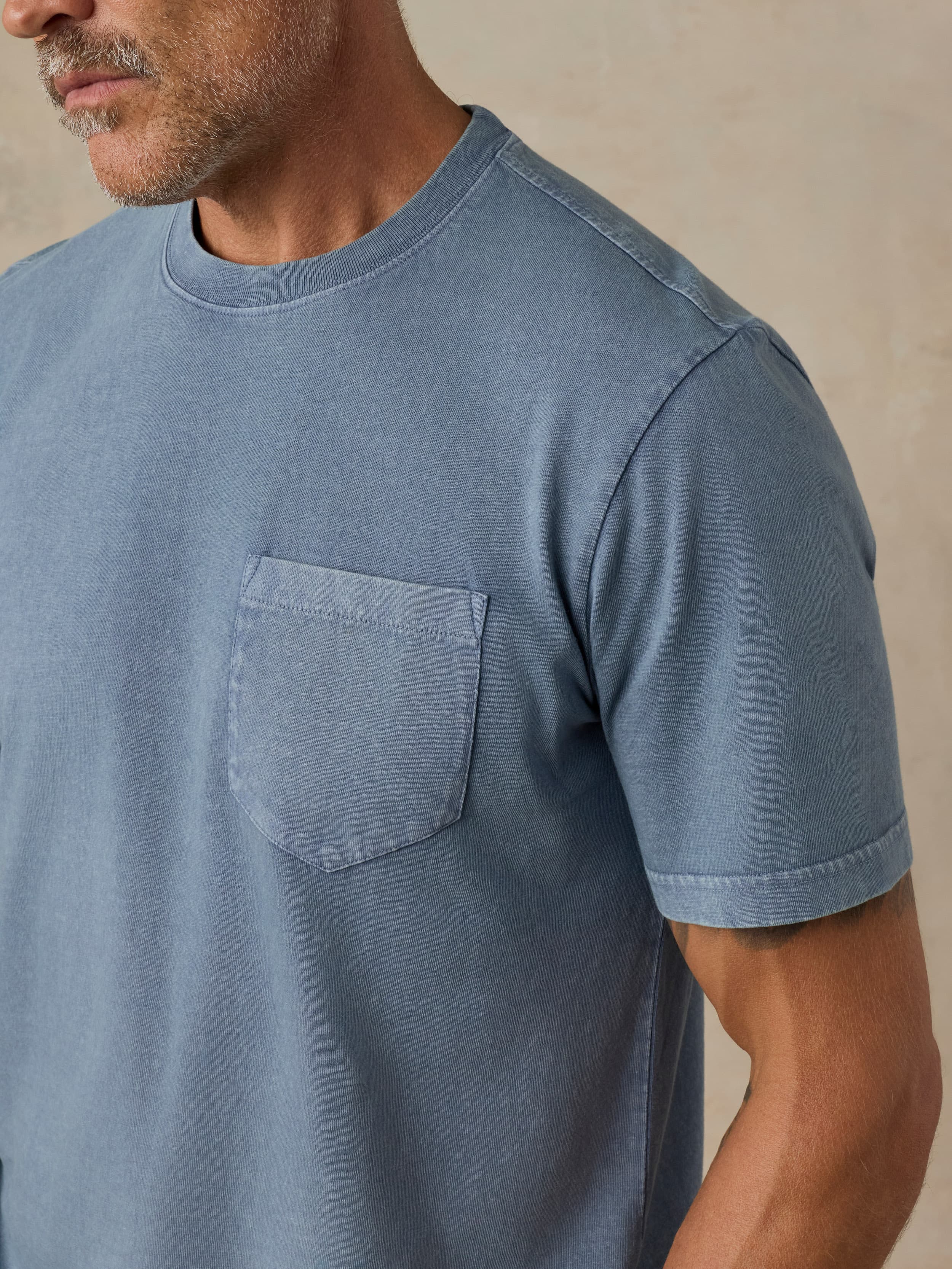 Man wearing a blue pocket tee against a beige background