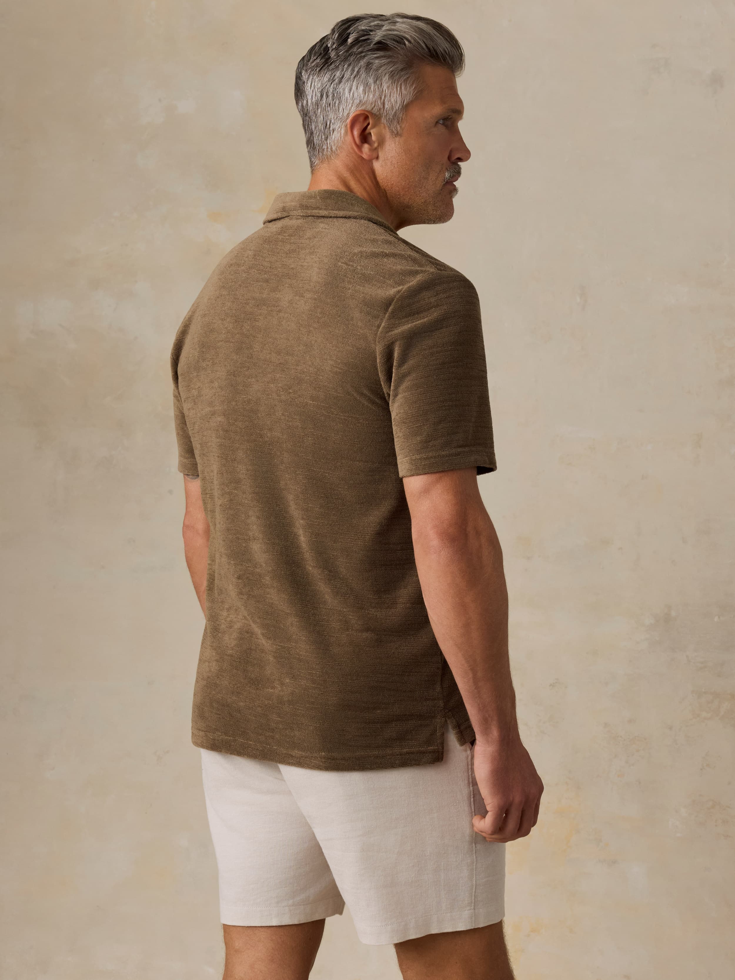 Man wearing a brown polo shirt with white stripes and beige shorts against a beige background