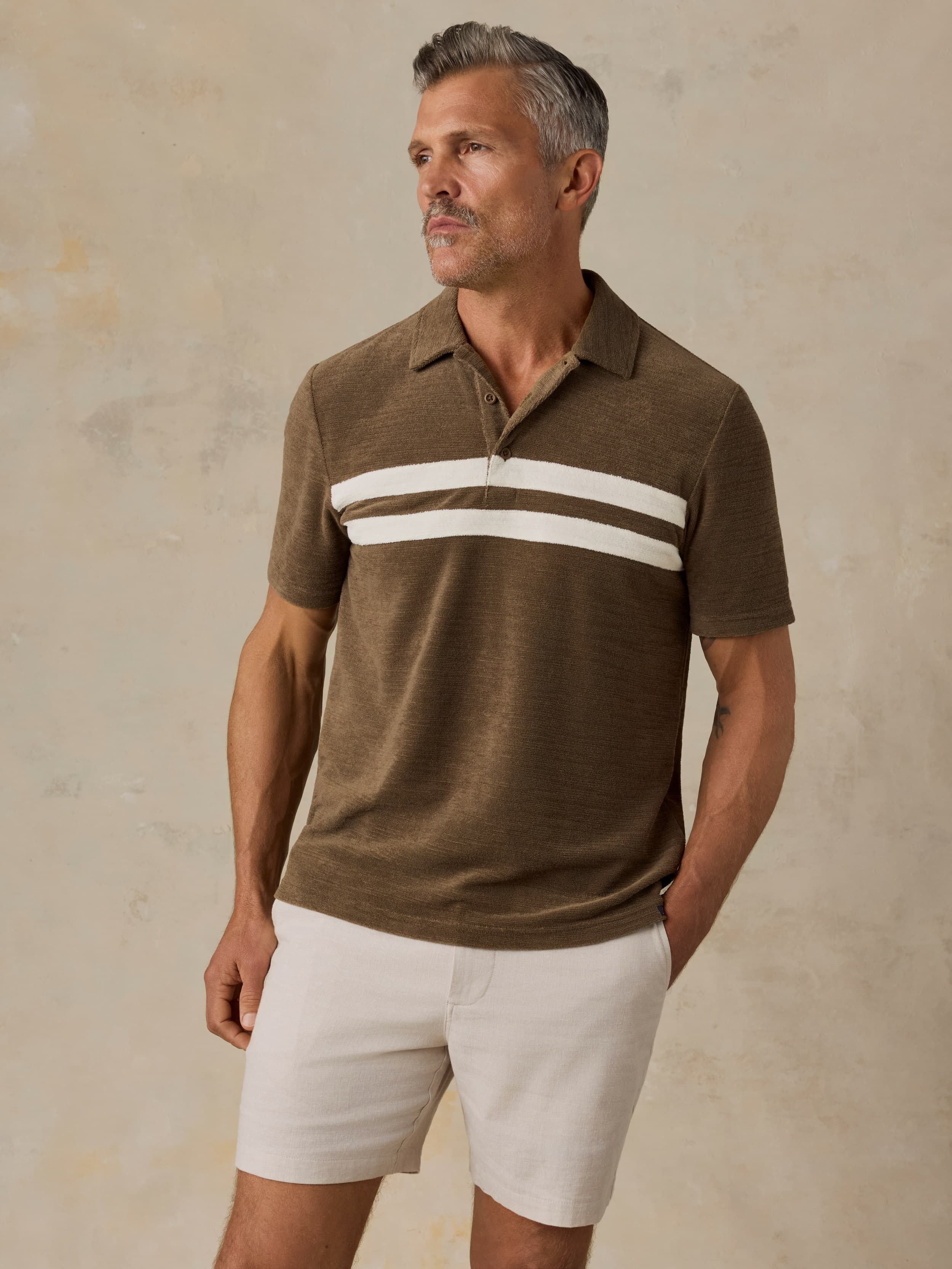Man wearing a brown polo shirt with white stripes and beige shorts against a beige background