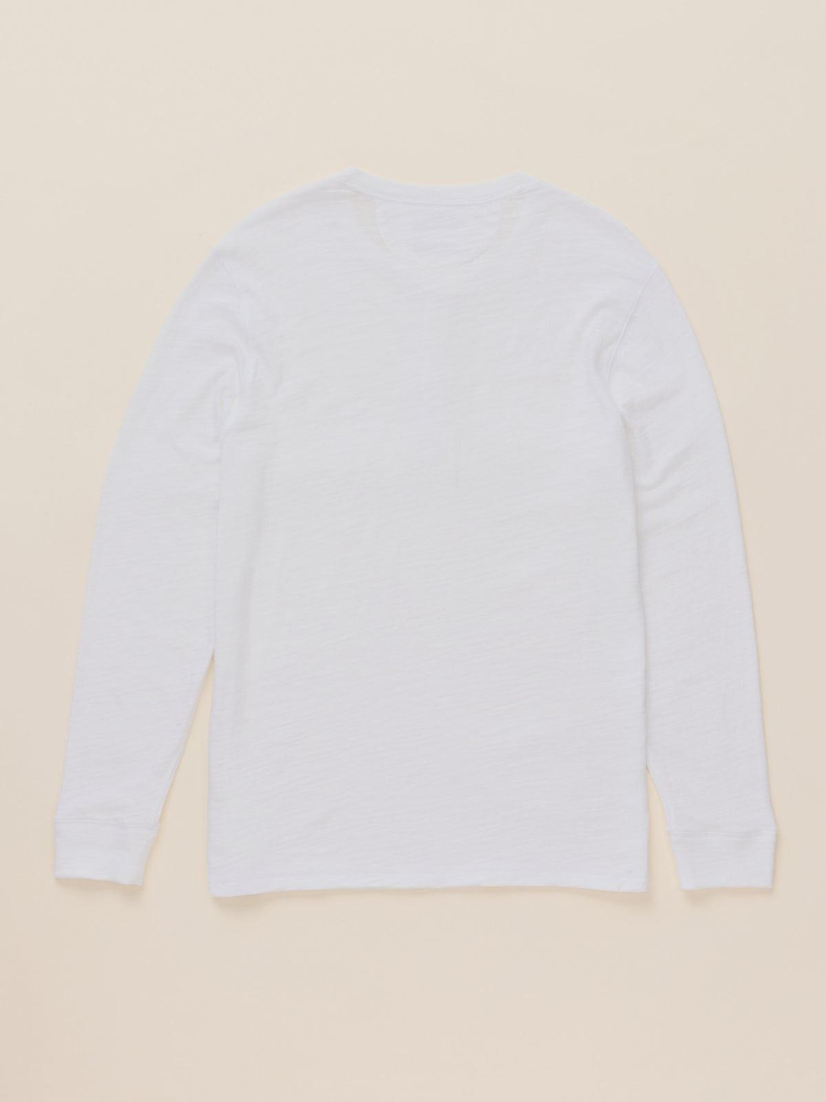 A plain white long-sleeve crewneck shirt laid flat against a light beige background.
