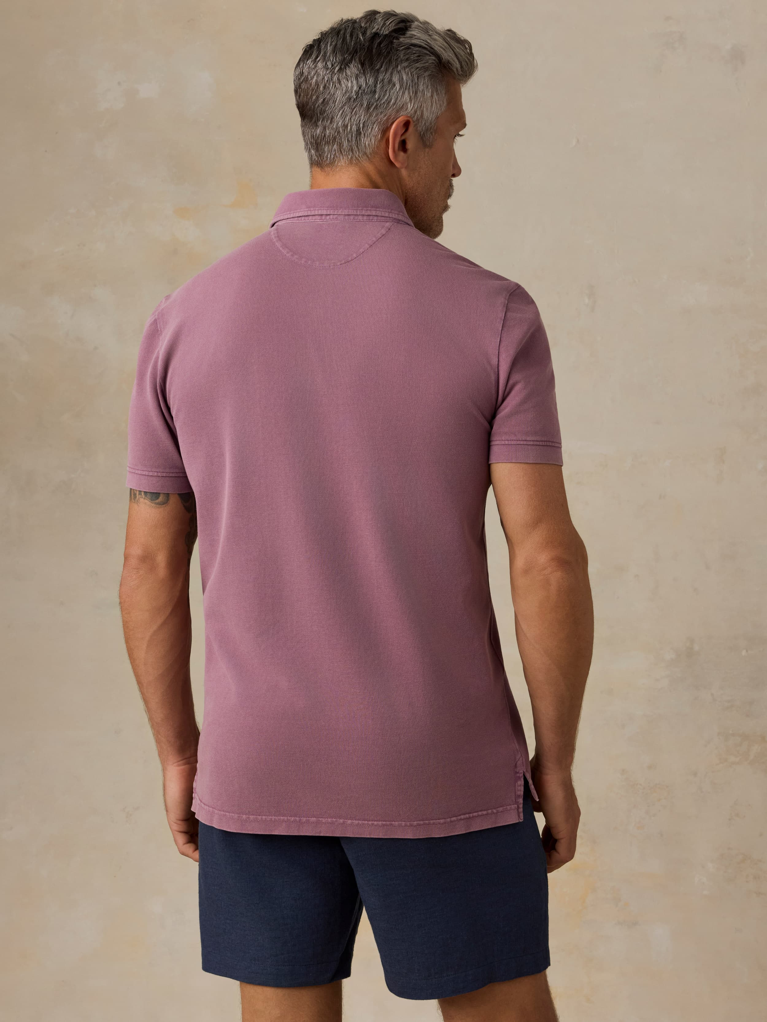 Man wearing a purple polo shirt and navy shorts against a beige background