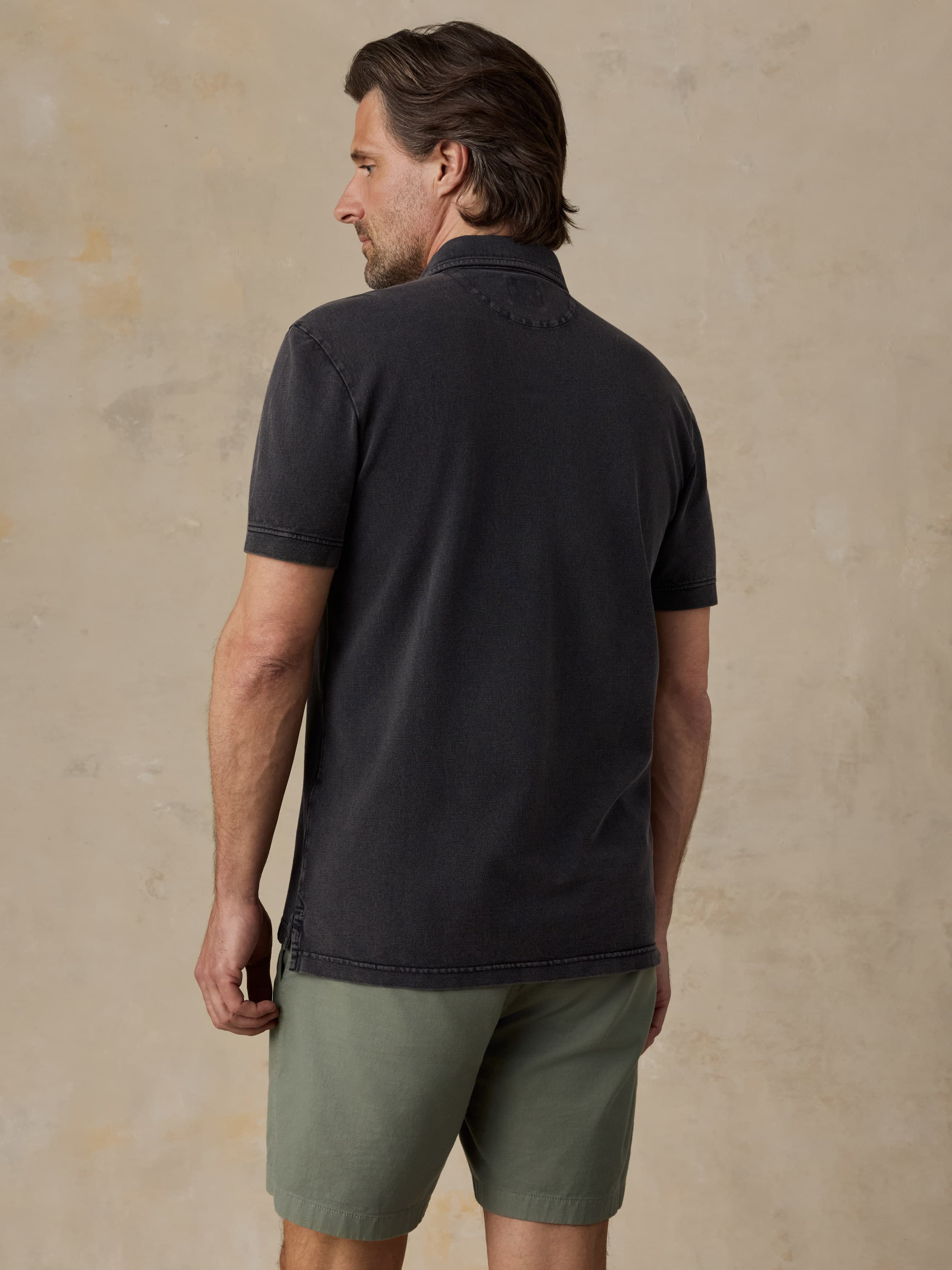 Man wearing a black polo shirt and green shorts against a beige background