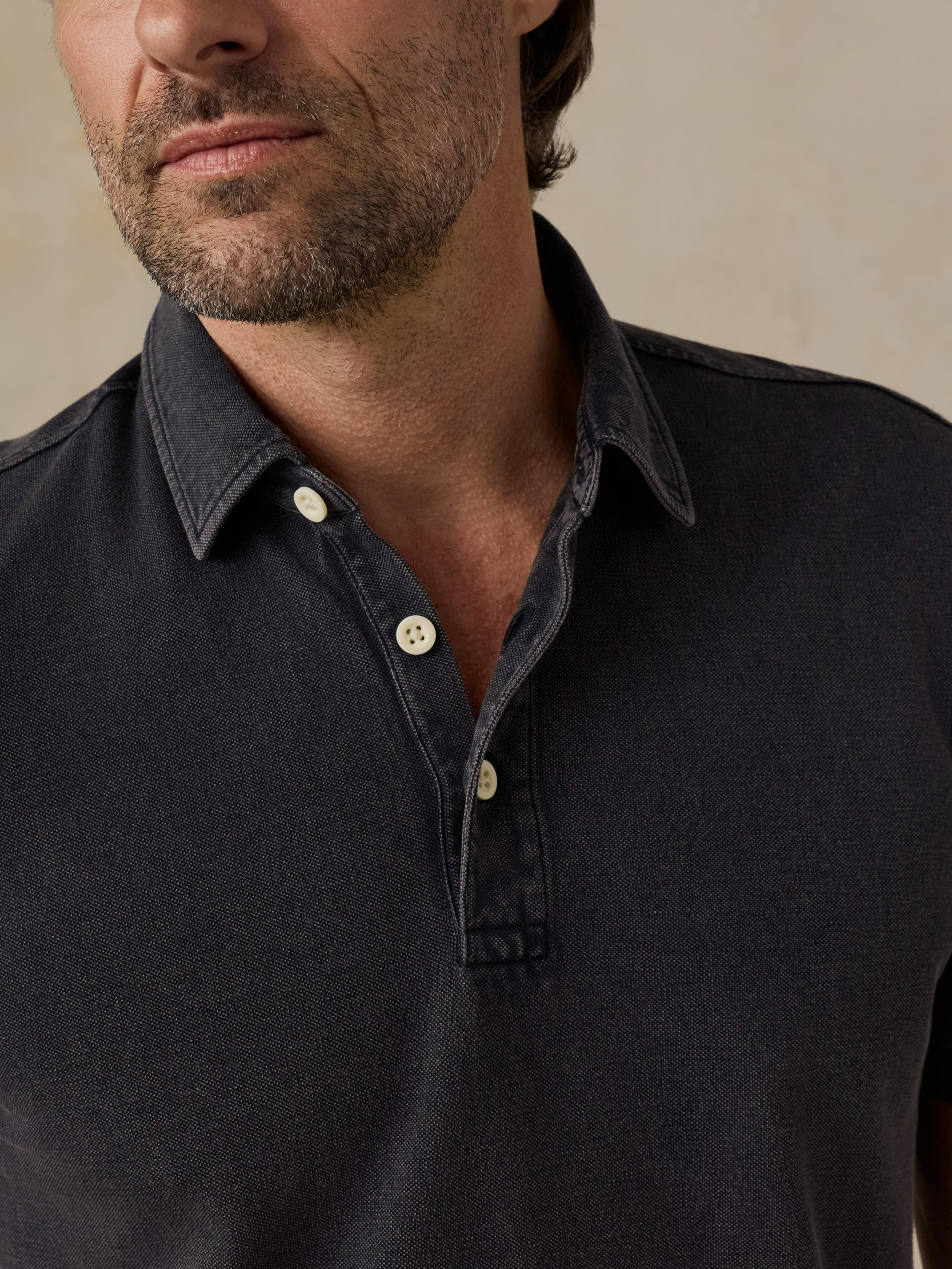 Man wearing a black polo shirt with a beige background