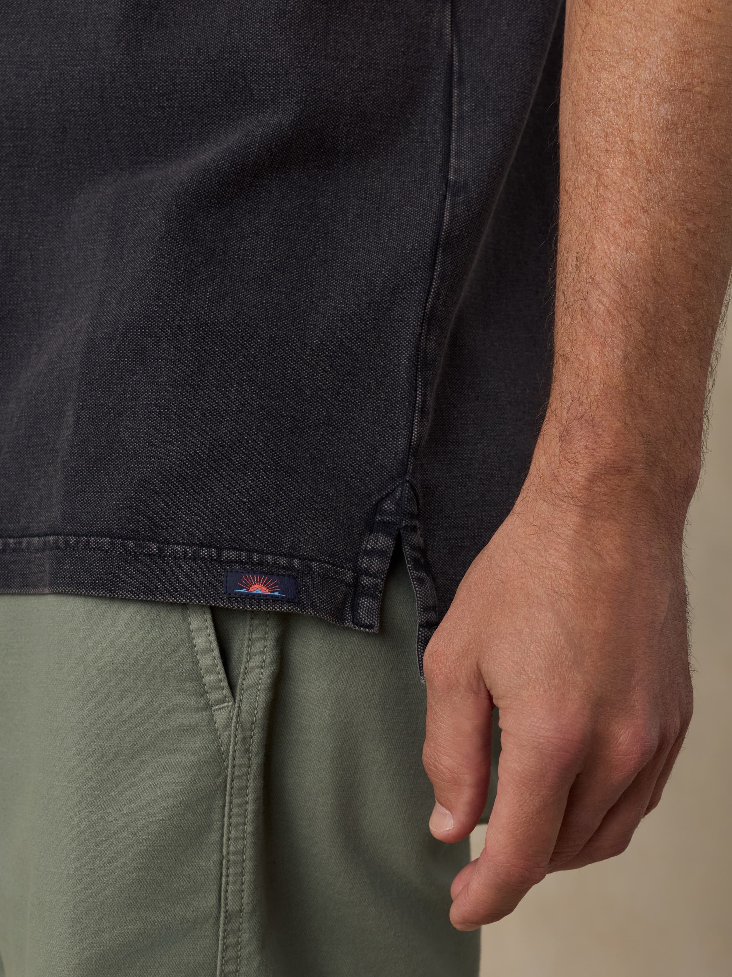 Man wearing a black polo shirt with a visible Faherty brand logo and green shorts.