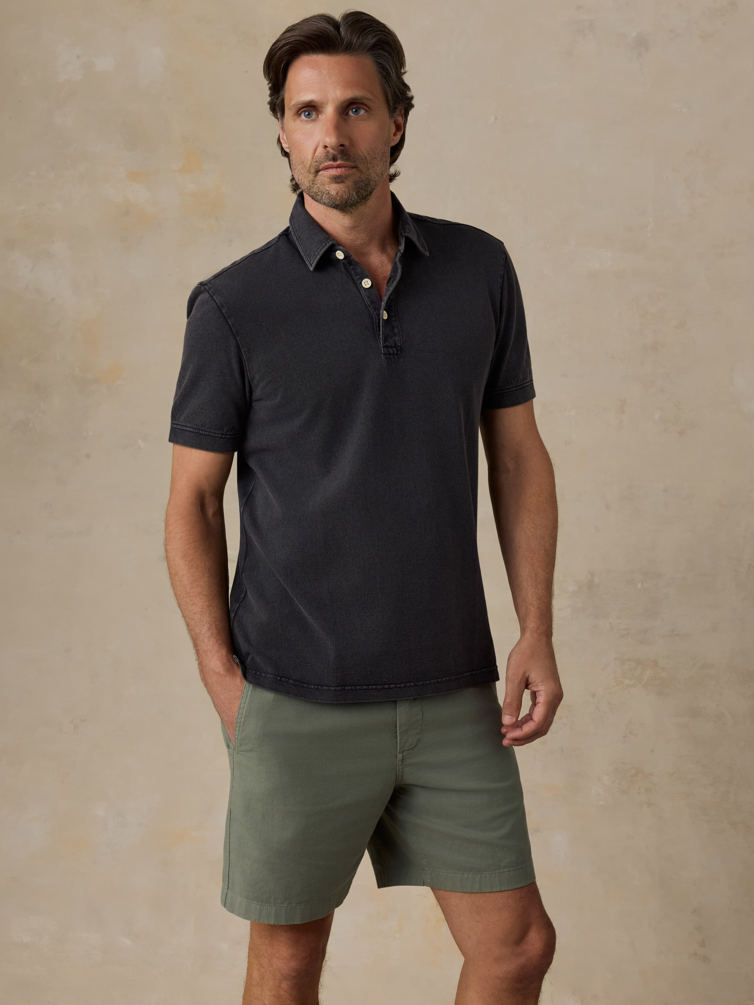 Man wearing a black polo shirt and green shorts against a beige background