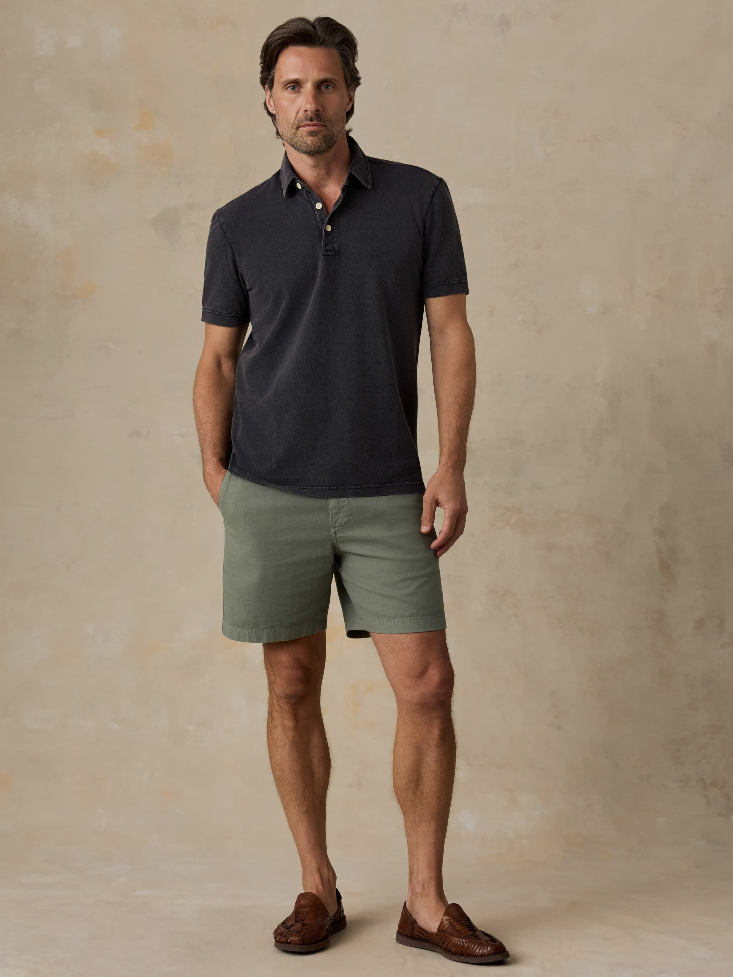 Man wearing a black polo shirt and green shorts against a beige background