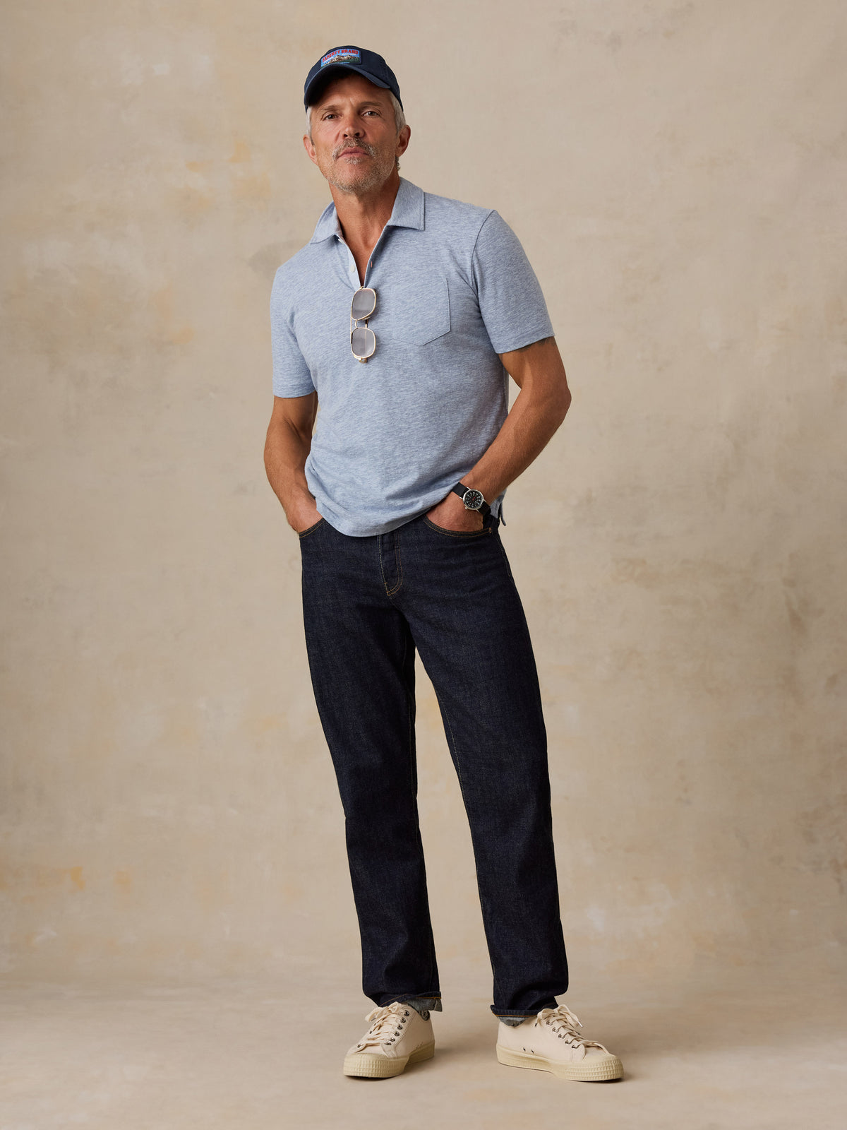 A man wearing a light blue polo and jeans, image 2 of 5