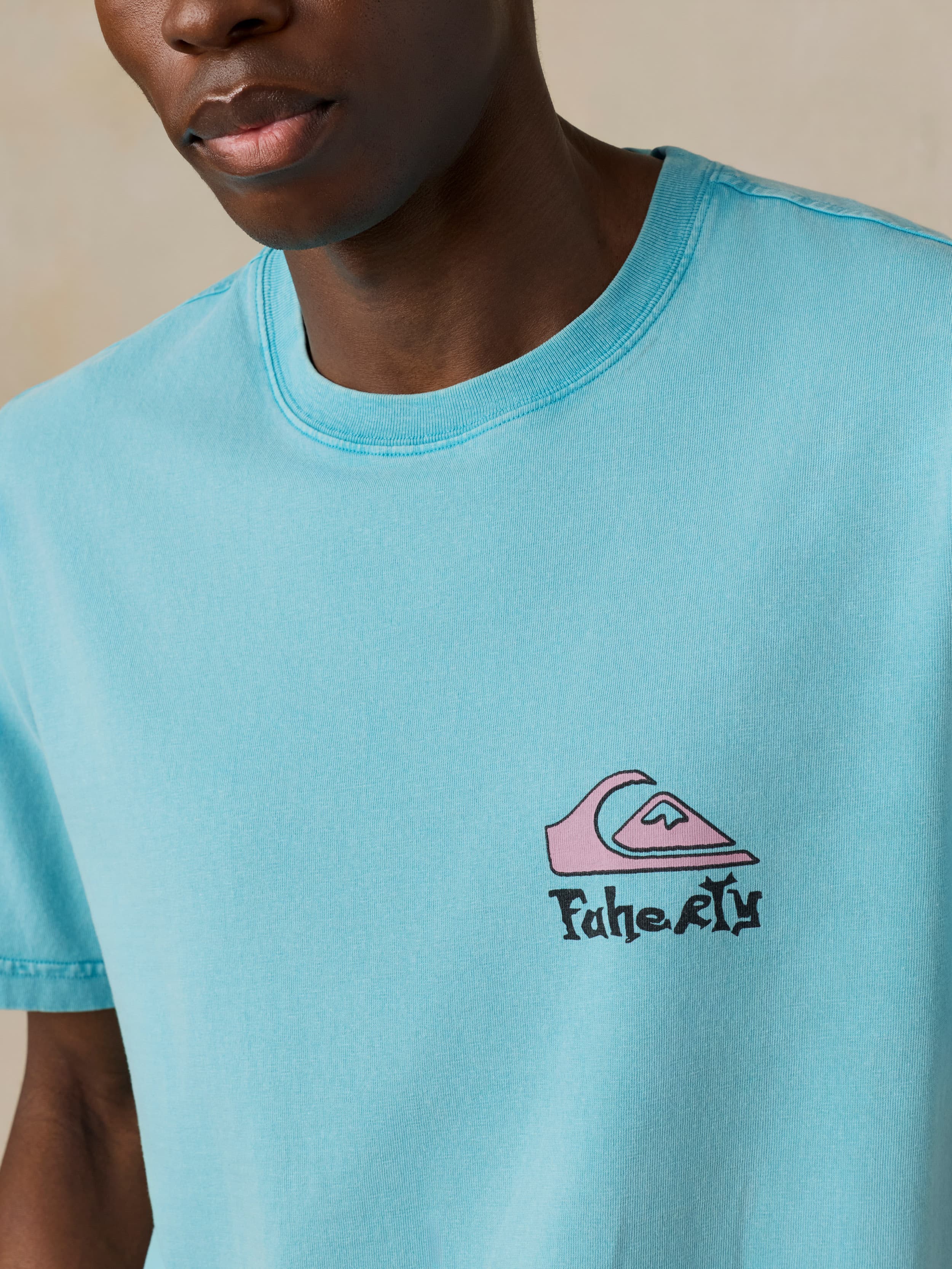 Man wearing a blue Faherty x Quiksilver tee against a beige background