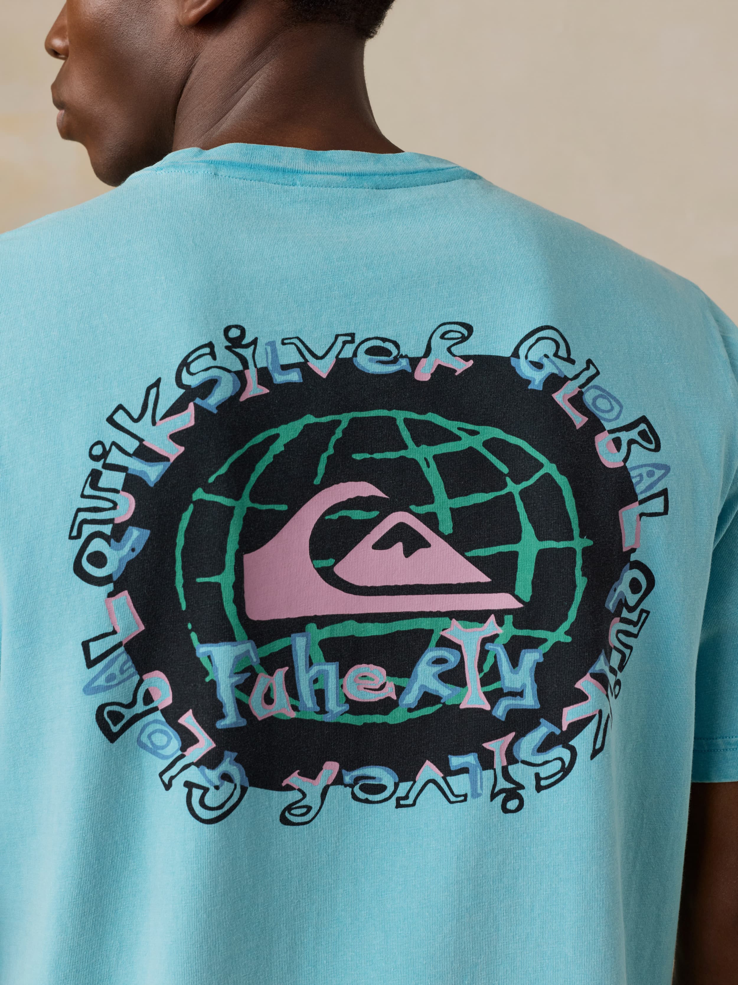 Man wearing a blue Faherty x Quiksilver tee against a beige background