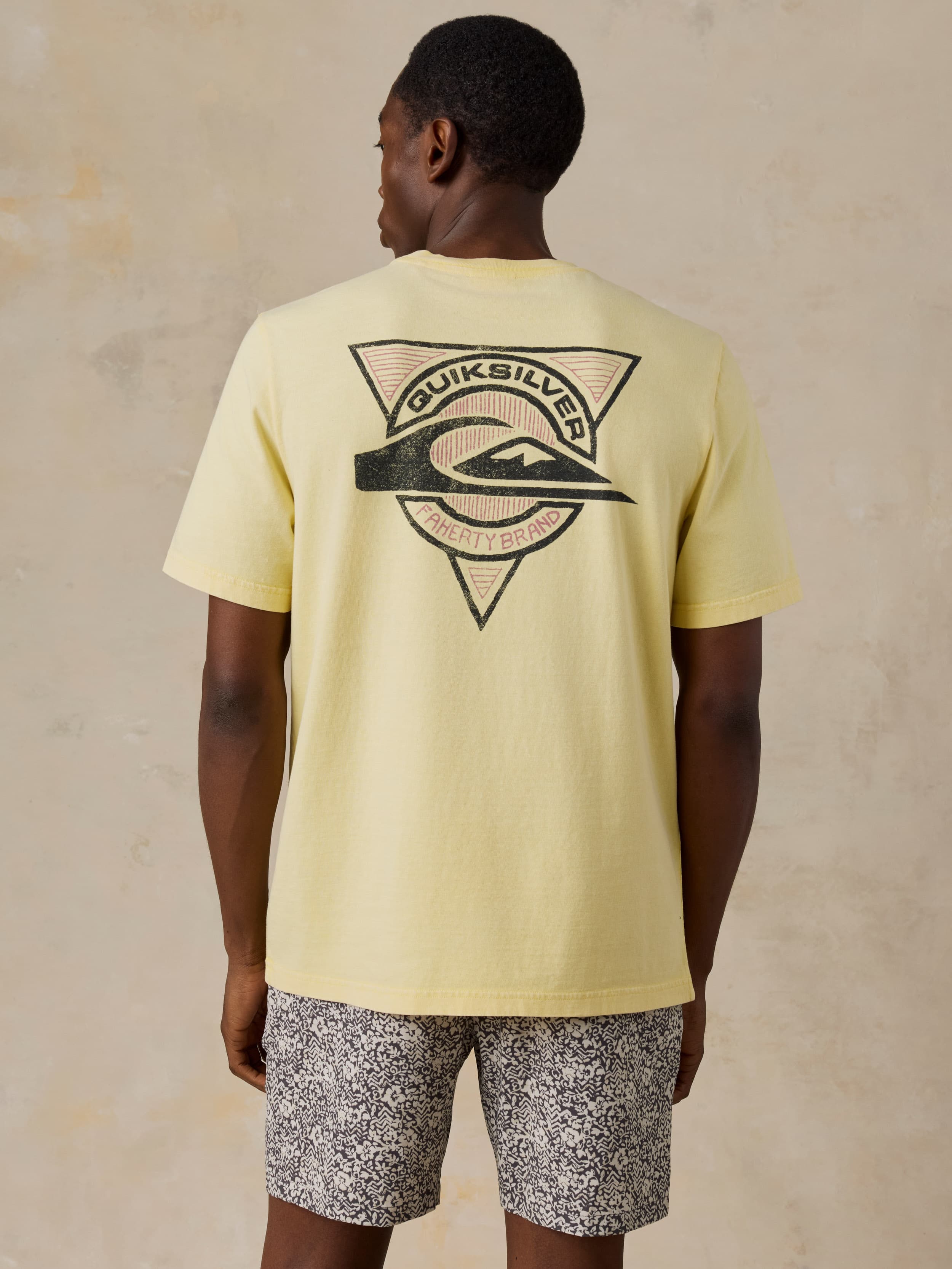 Man wearing a yellow Faherty x Quiksilver tee and printed shorts against a beige background