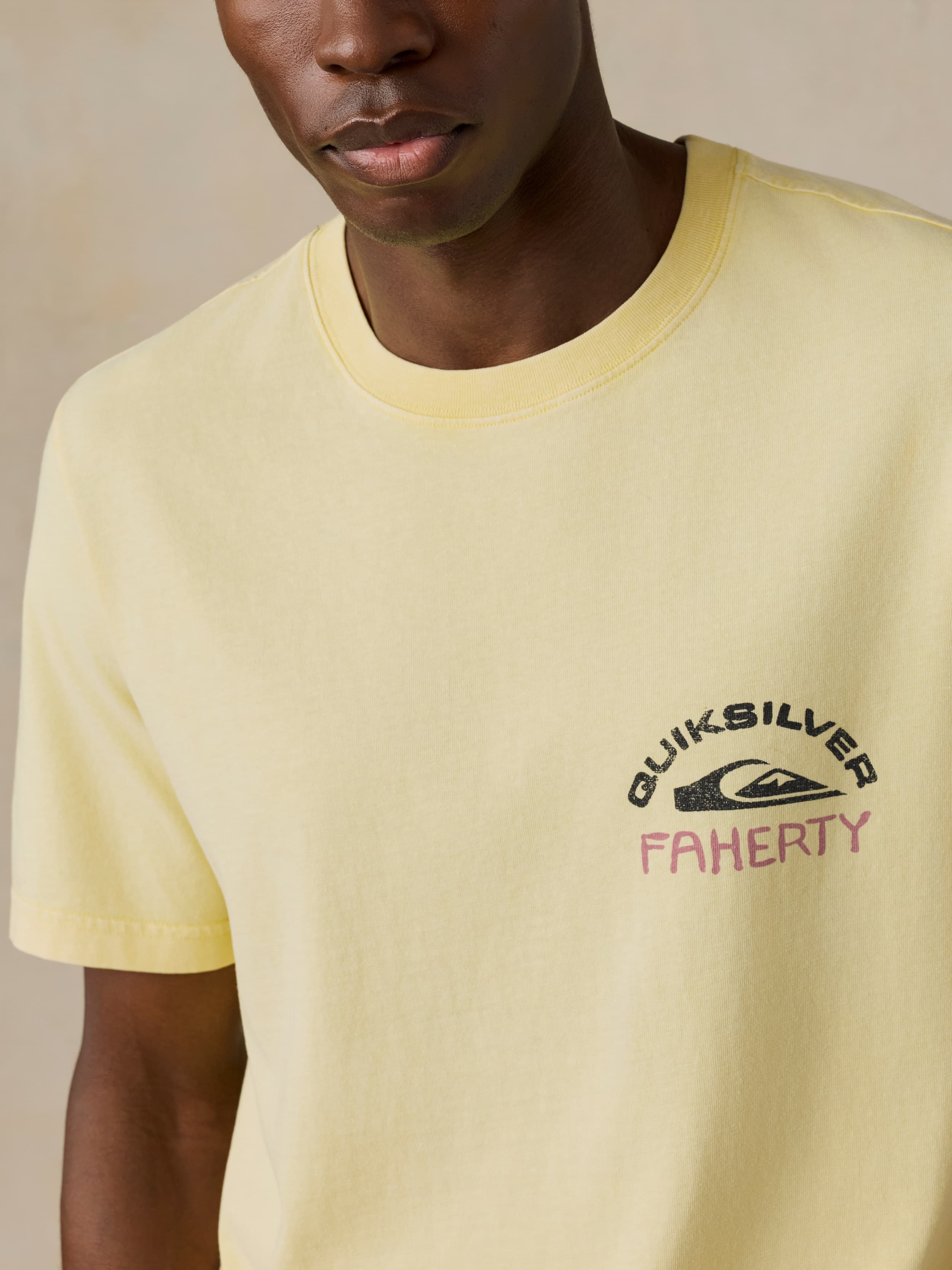 Man wearing a yellow Faherty x Quiksilver tee against a beige background