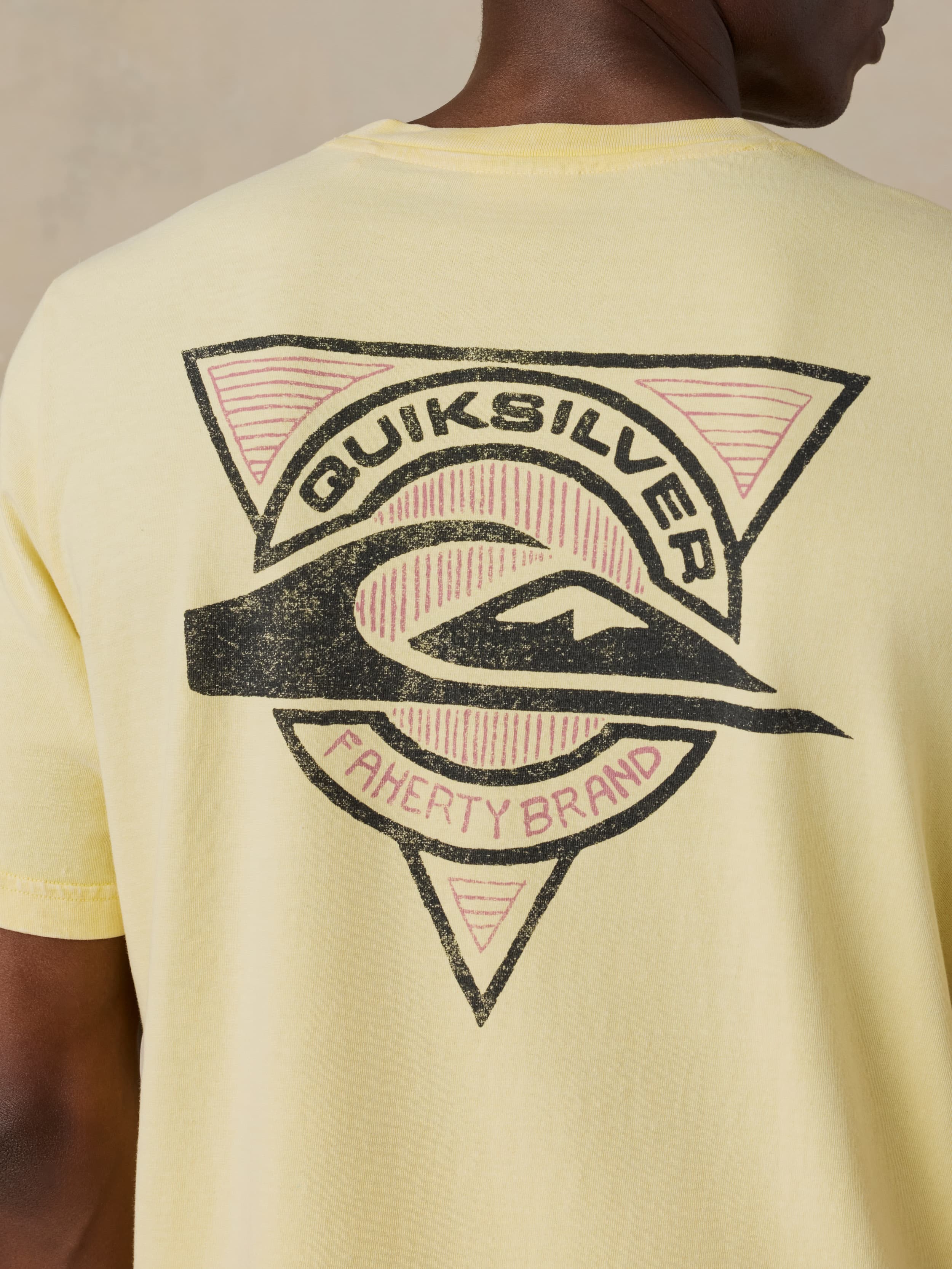 Man wearing a yellow Faherty x Quiksilver tee against a beige background