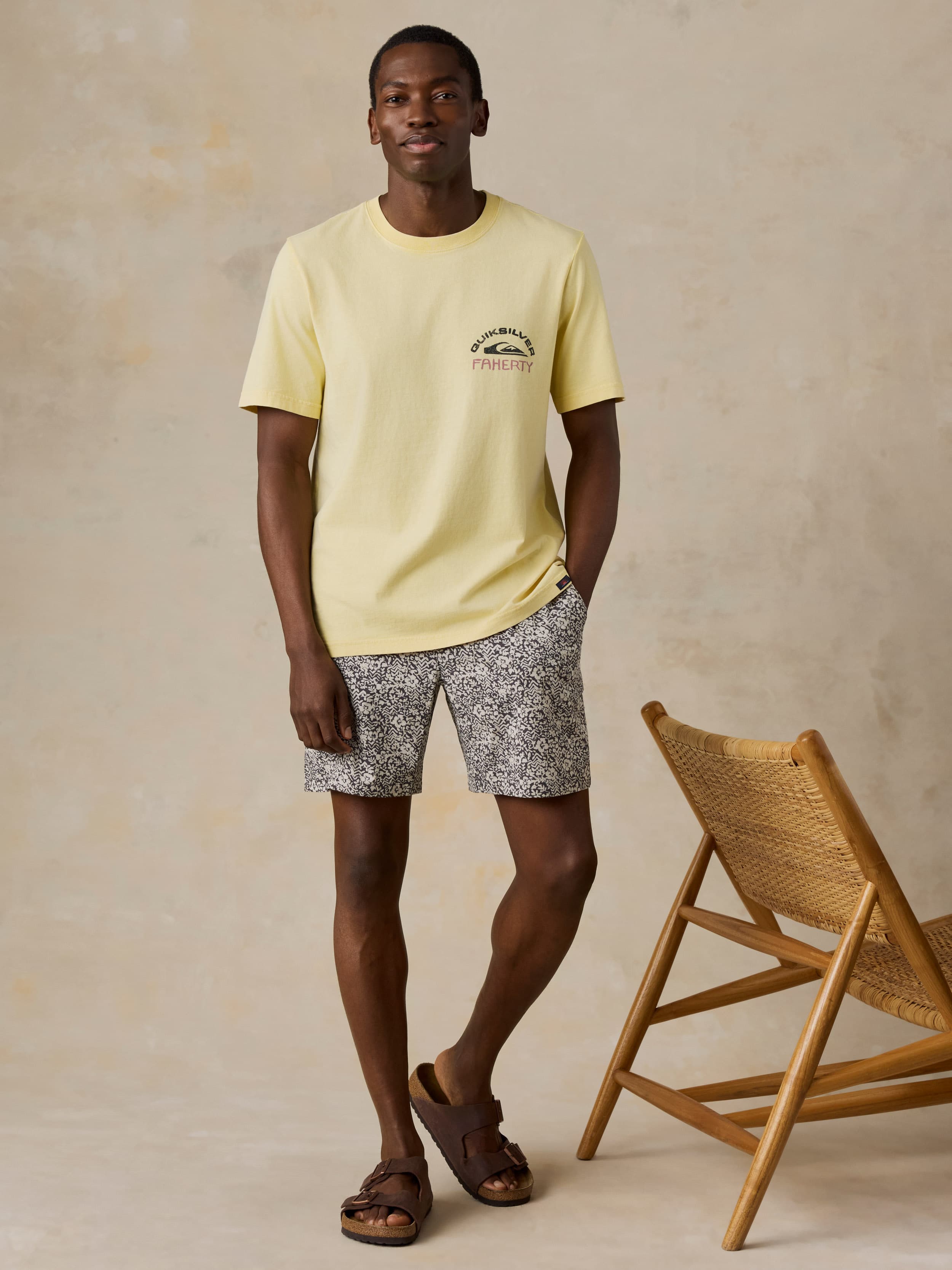 Man wearing a yellow Faherty x Quiksilver tee and printed shorts against a beige background