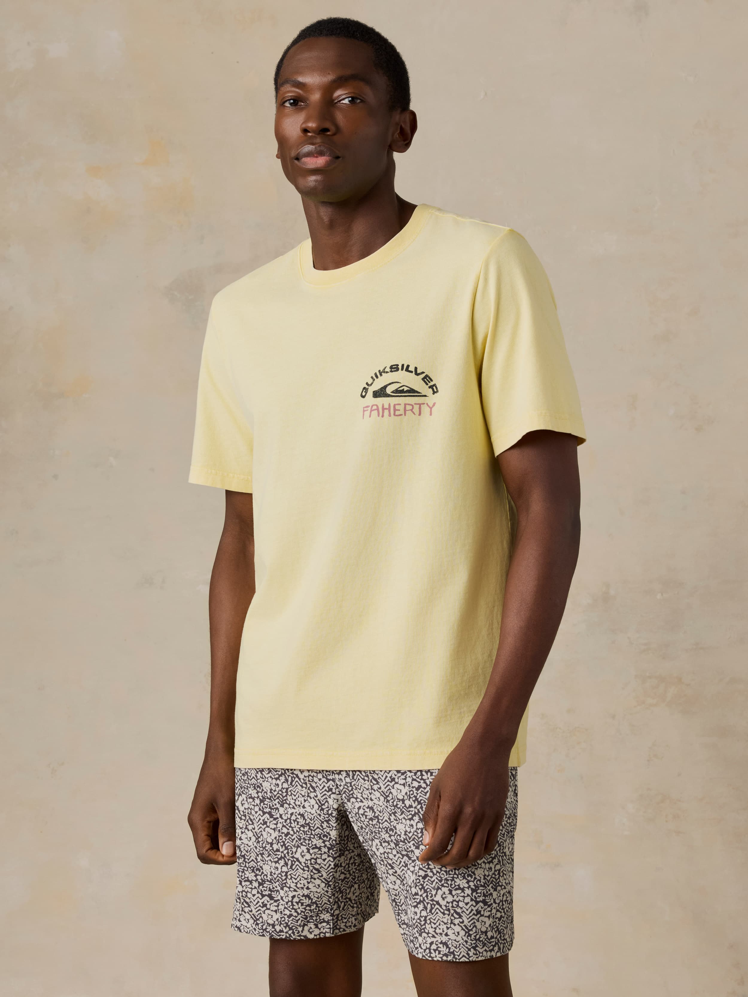 Man wearing a yellow Faherty x Quiksilver tee and printed shorts against a beige background