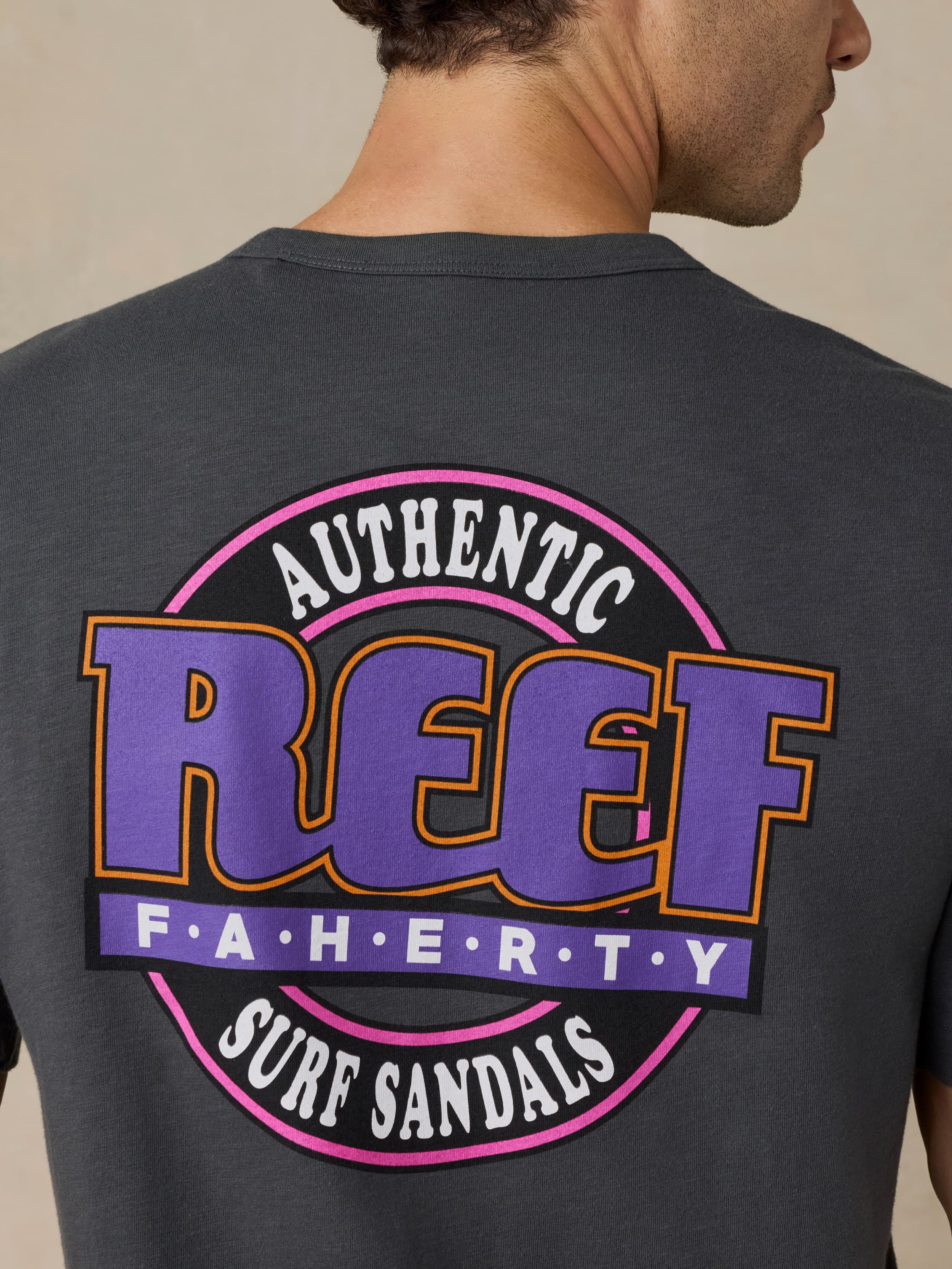 Man wearing a dark gray t-shirt with a Faherty x REEF logo on a beige background