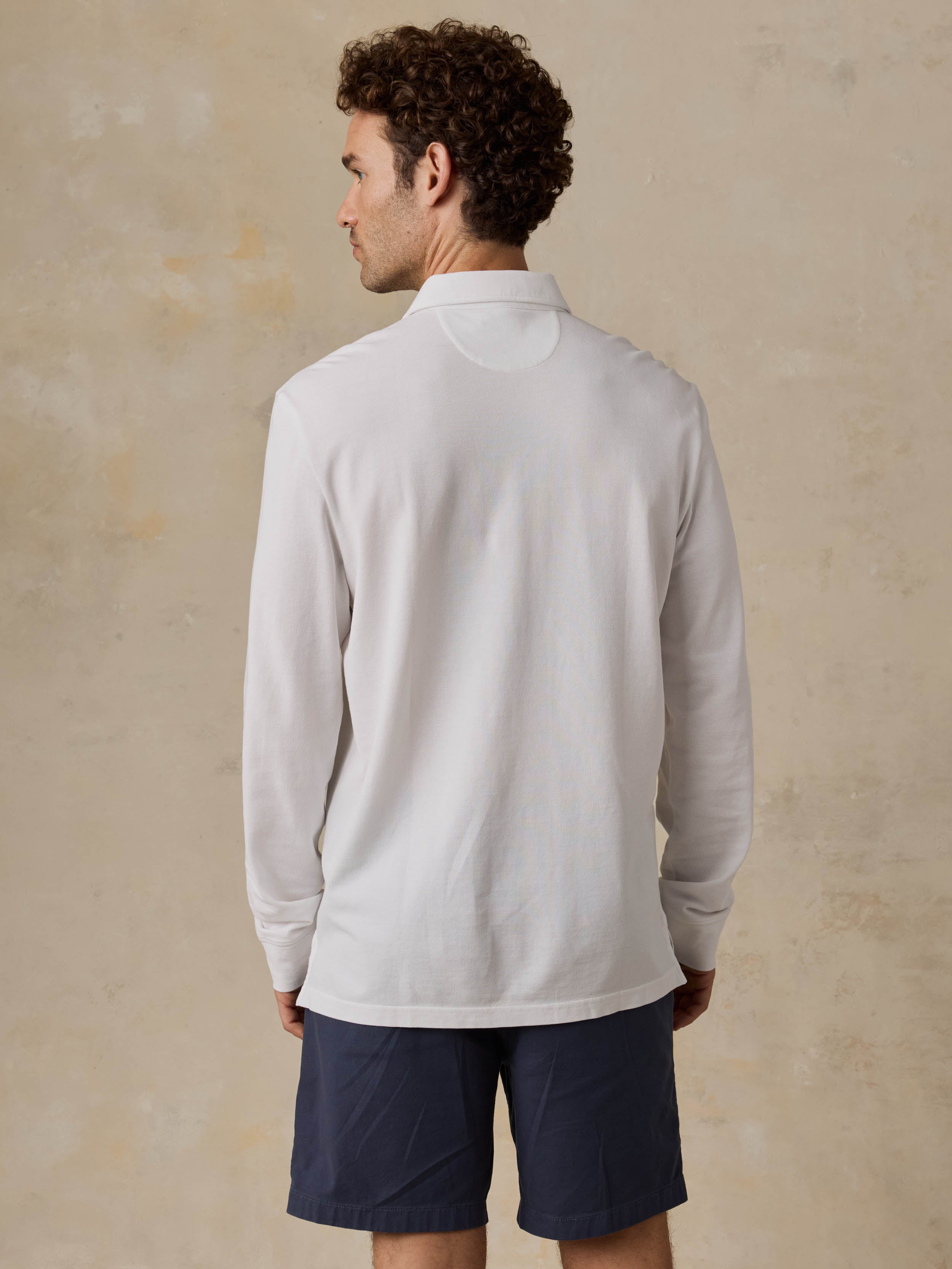 Man wearing a white long-sleeve polo shirt and navy shorts against a beige background