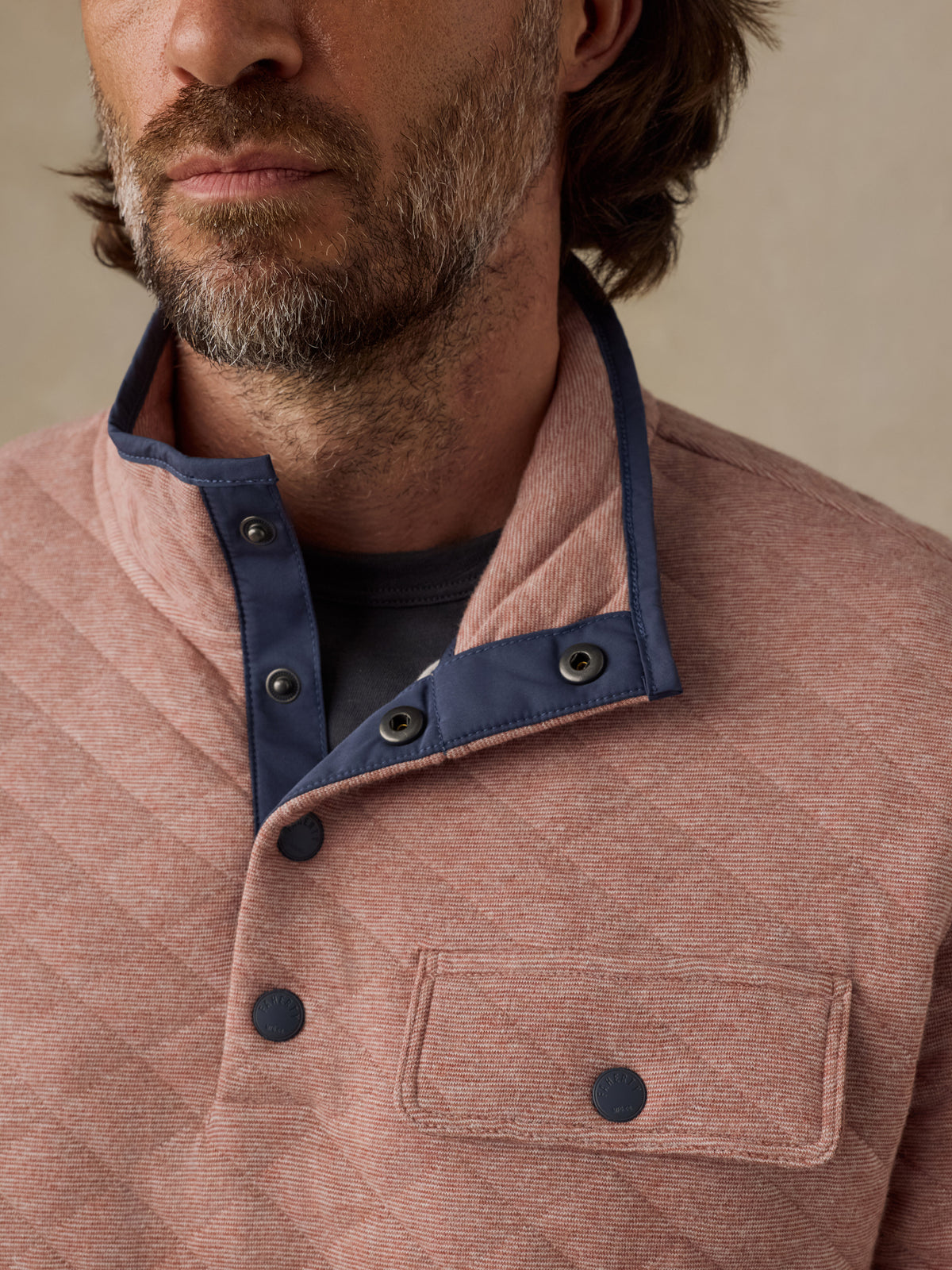 Close-up of a man wearing a quilted dusty rose corduroy jacket with a navy blue snap-button collar over a dark shirt., image 3 of 5