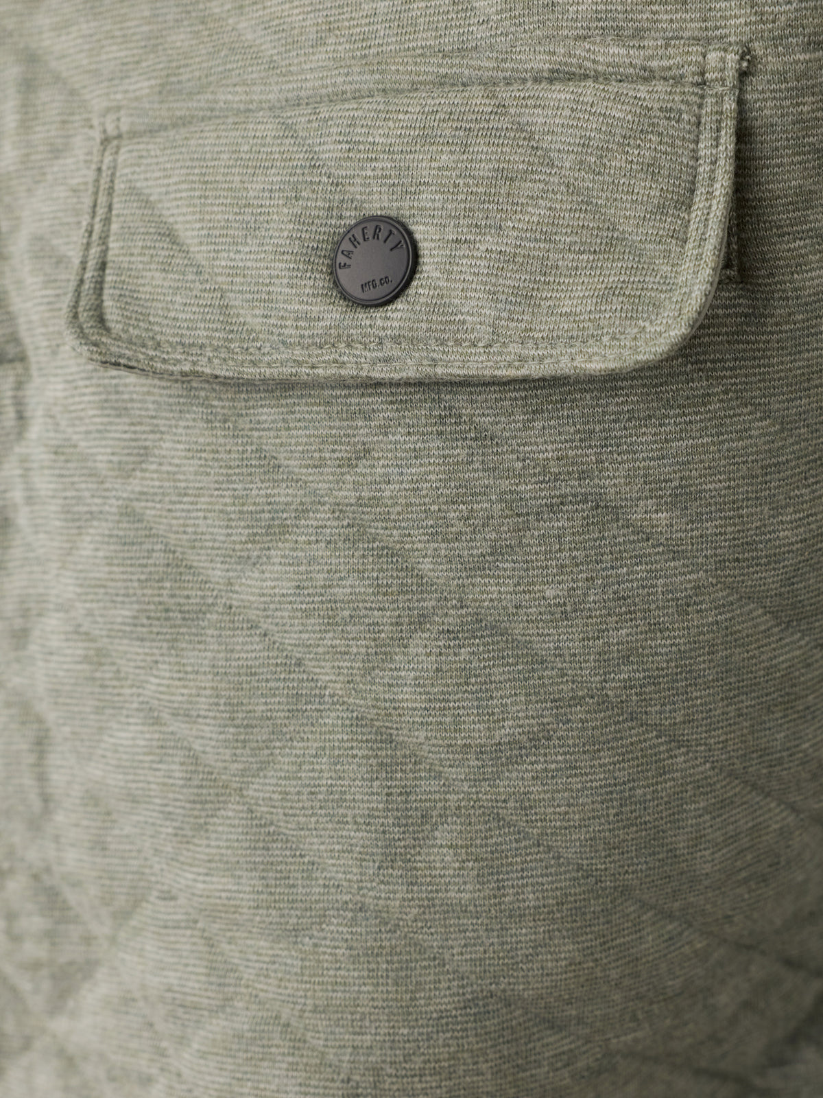 Close-up of a quilted light green fabric jacket with a flap pocket and a round dark gray button featuring the Faherty brand logo., image 5 of 6