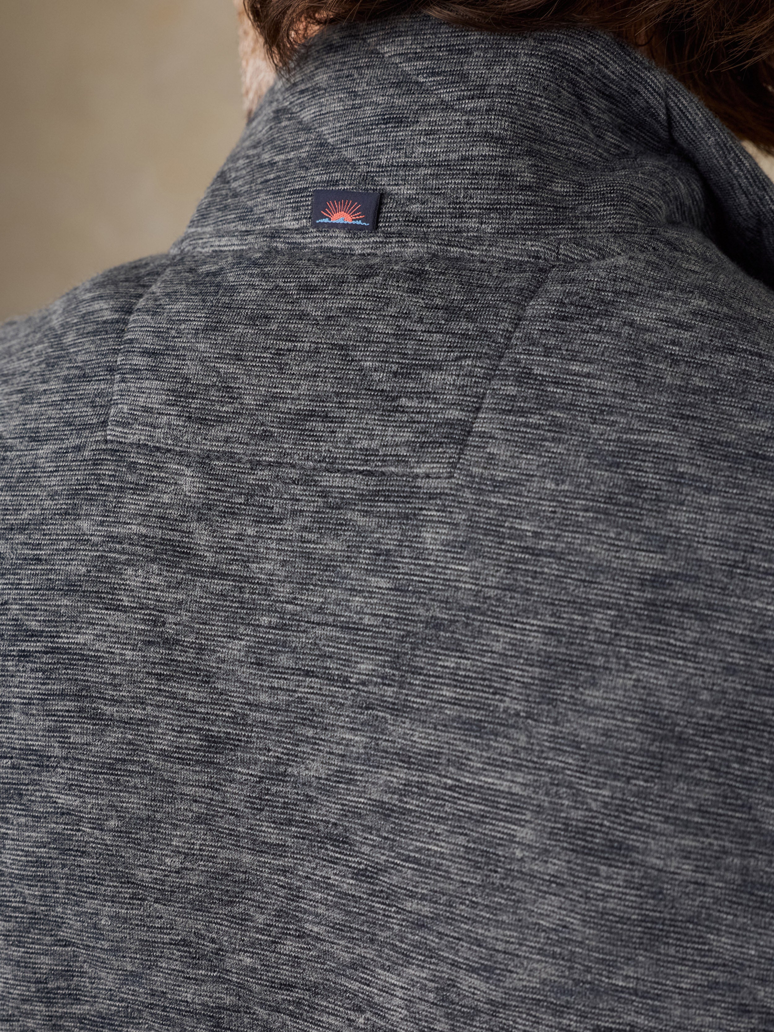 Close-up of the back of a dark gray heathered knit sweater or jacket, showing a small rectangular Faherty brand patch near the collar.
